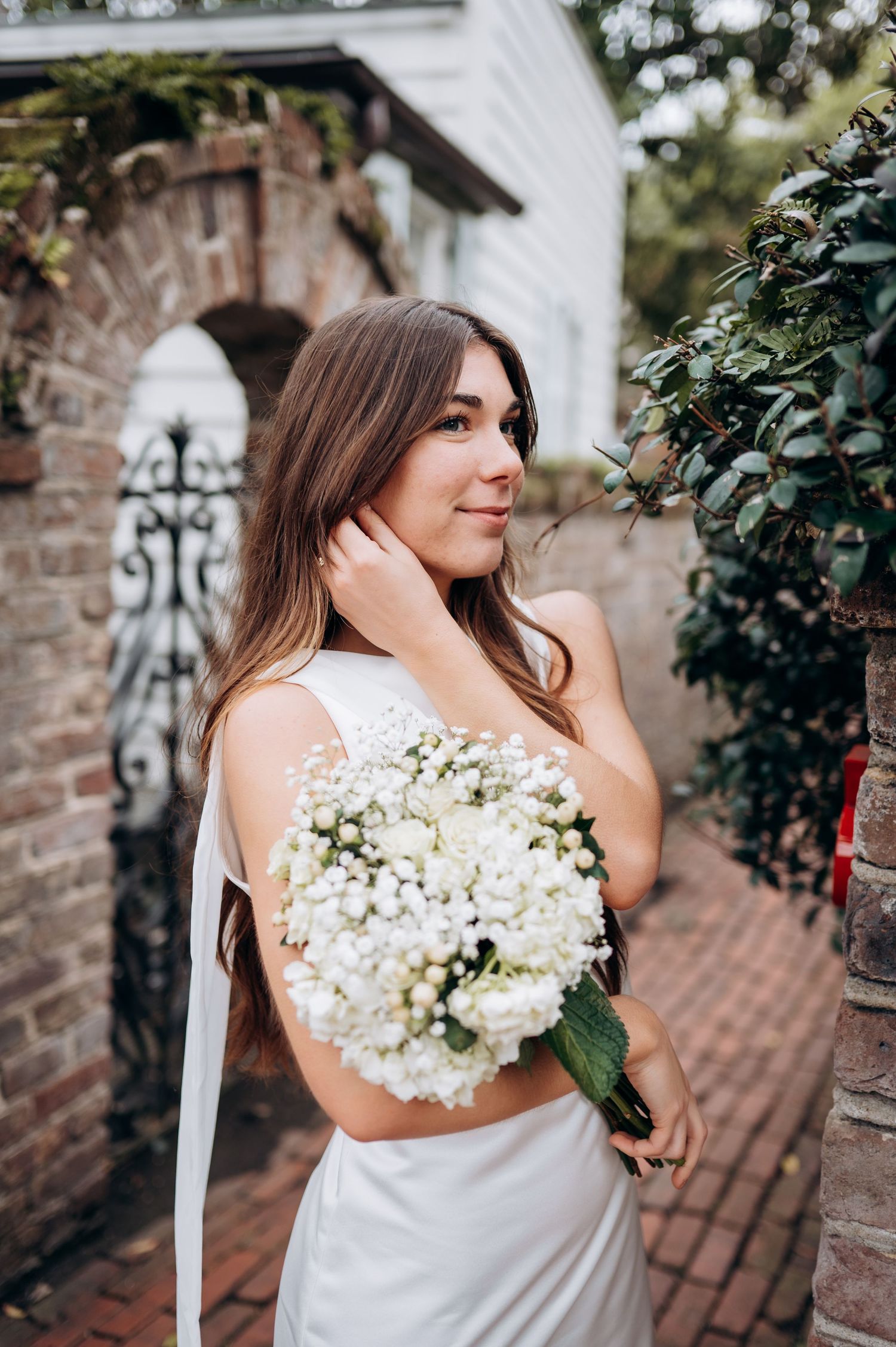 Bride holding a white hydrangea and baby's breath bouquet beside an iron gate and brick wall.