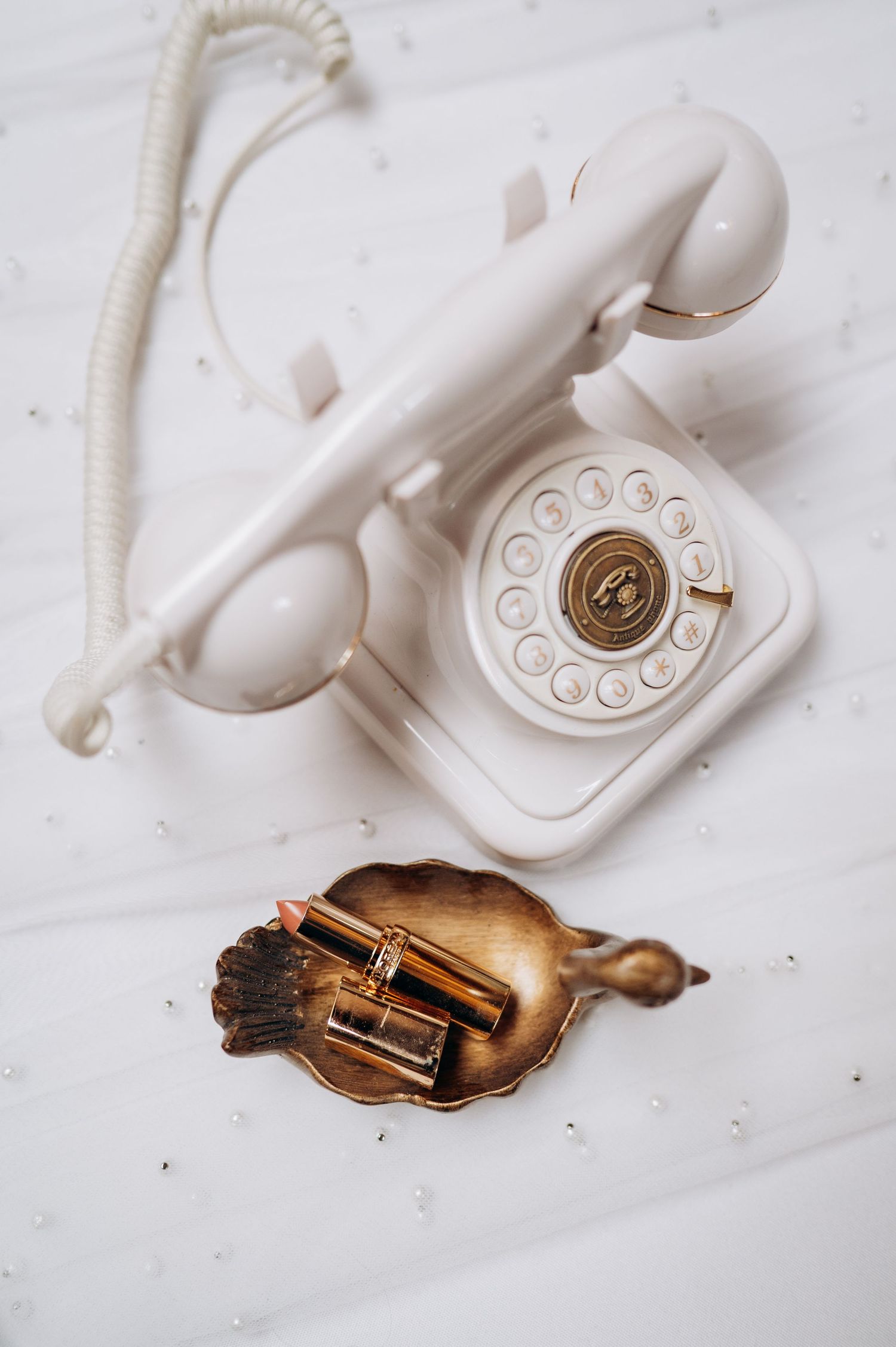 A vintage white rotary telephone sits beside a decorative brass or copper dish with cinnamon sticks.