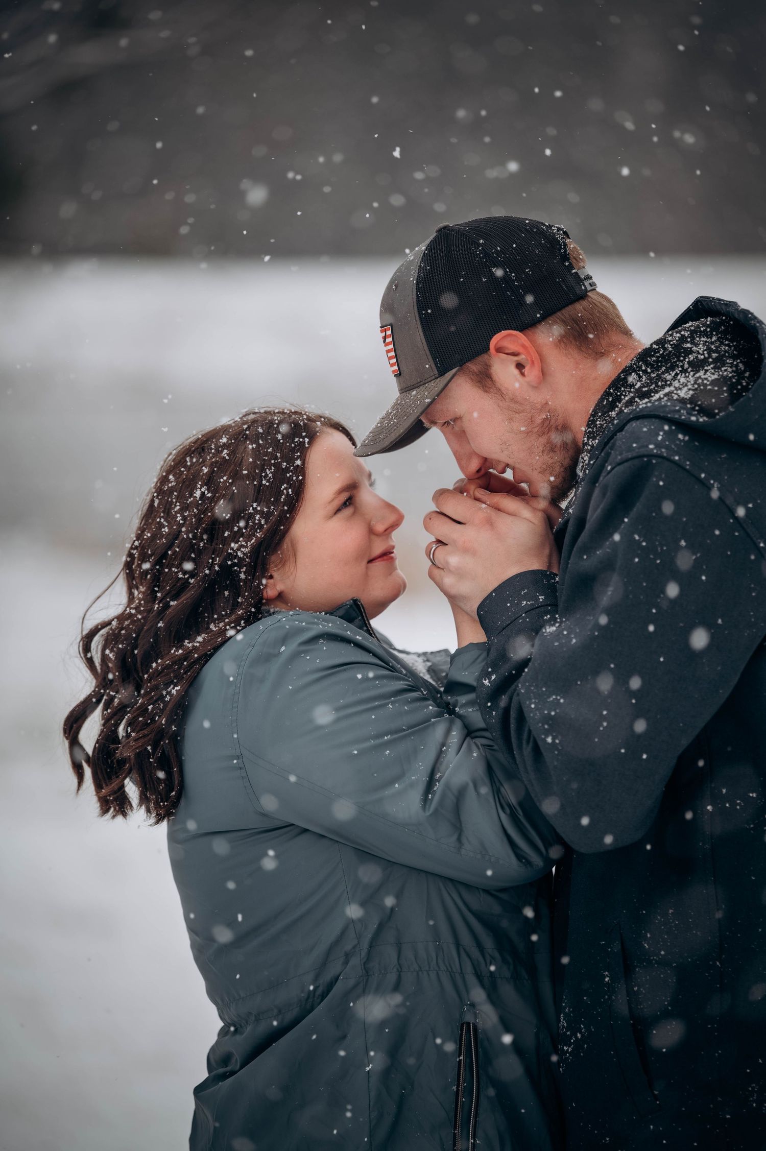 A romantic couple shares intimate moments in the falling snow while wearing winter coats.