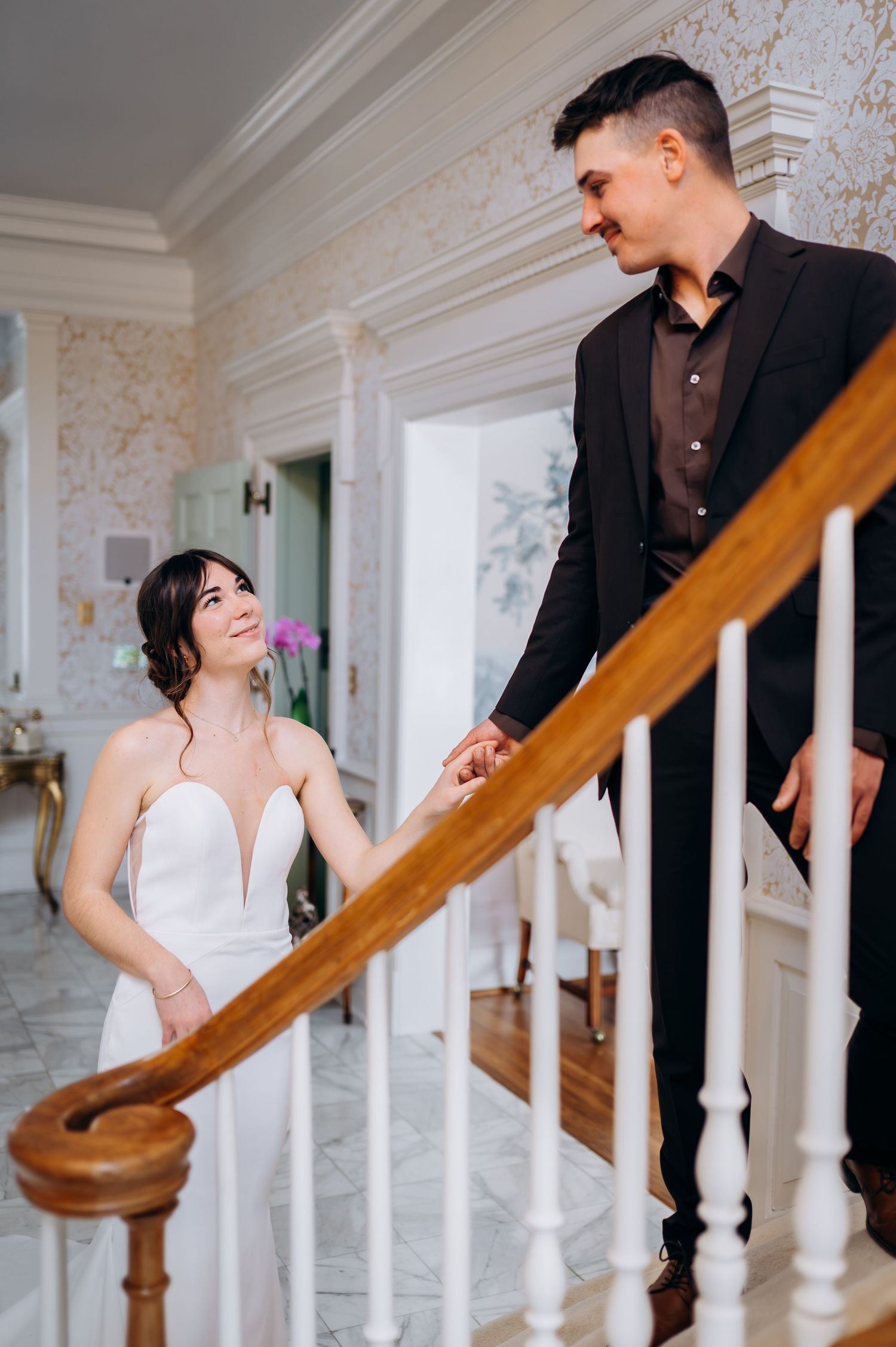 Romantic couple shares playful moments on an elegant staircase with white columns and wooden railings.