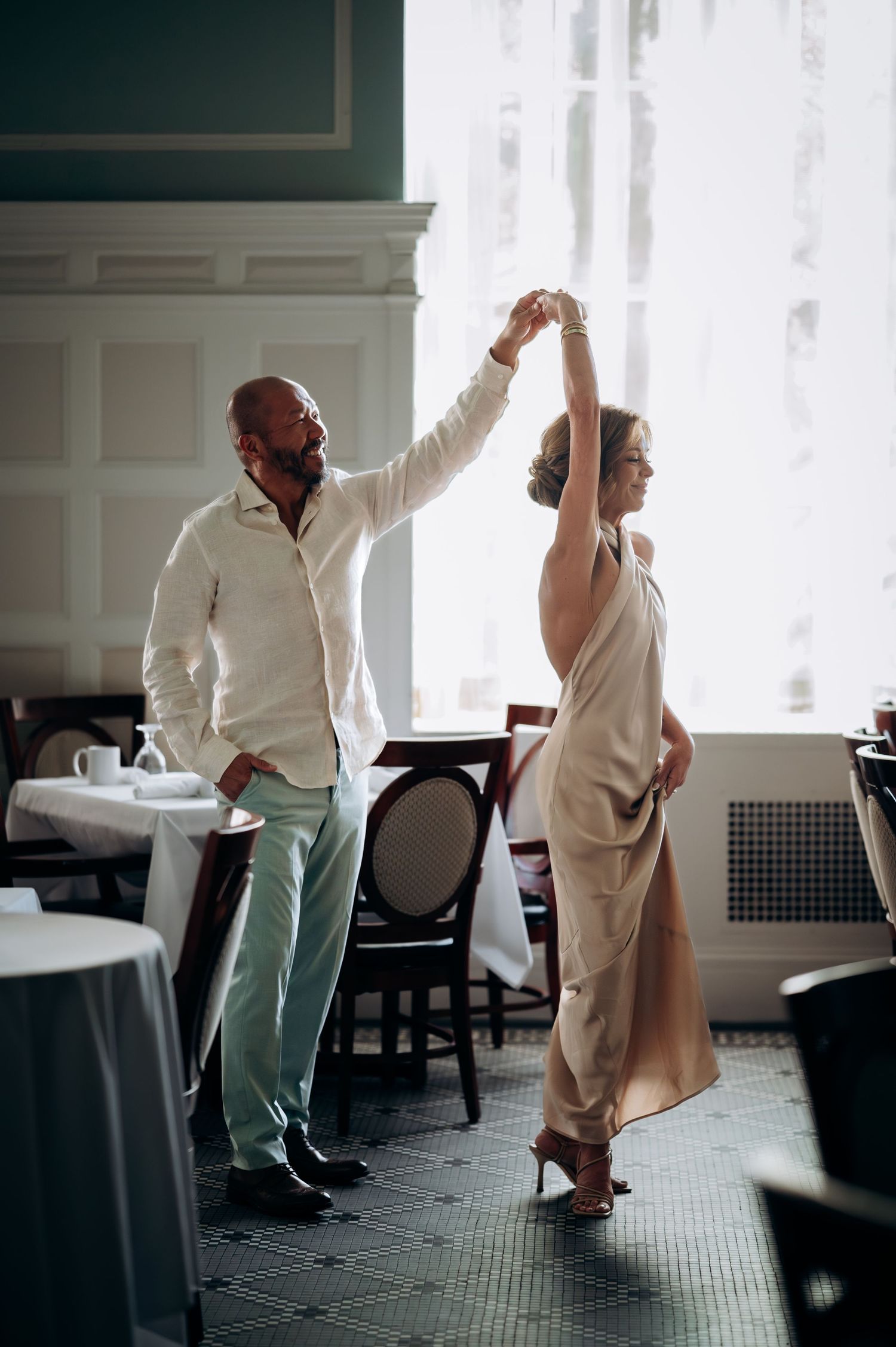 Couple dancing together in an elegant restaurant, man spinning woman in gold dress.