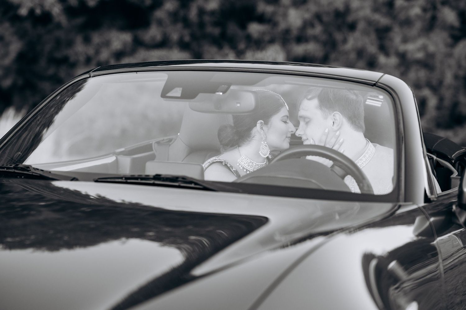Black and white photo of a couple sharing a romantic moment inside a convertible car.