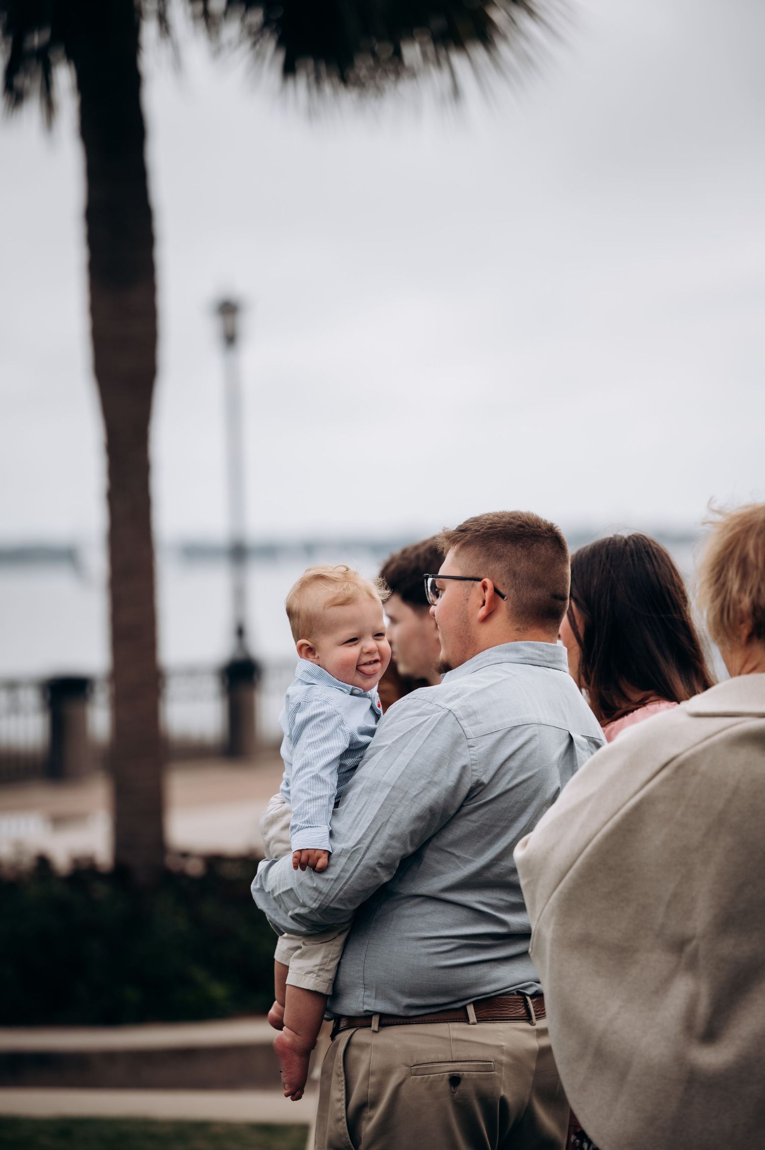 A touching family moment captured by the waterfront under a palm tree.