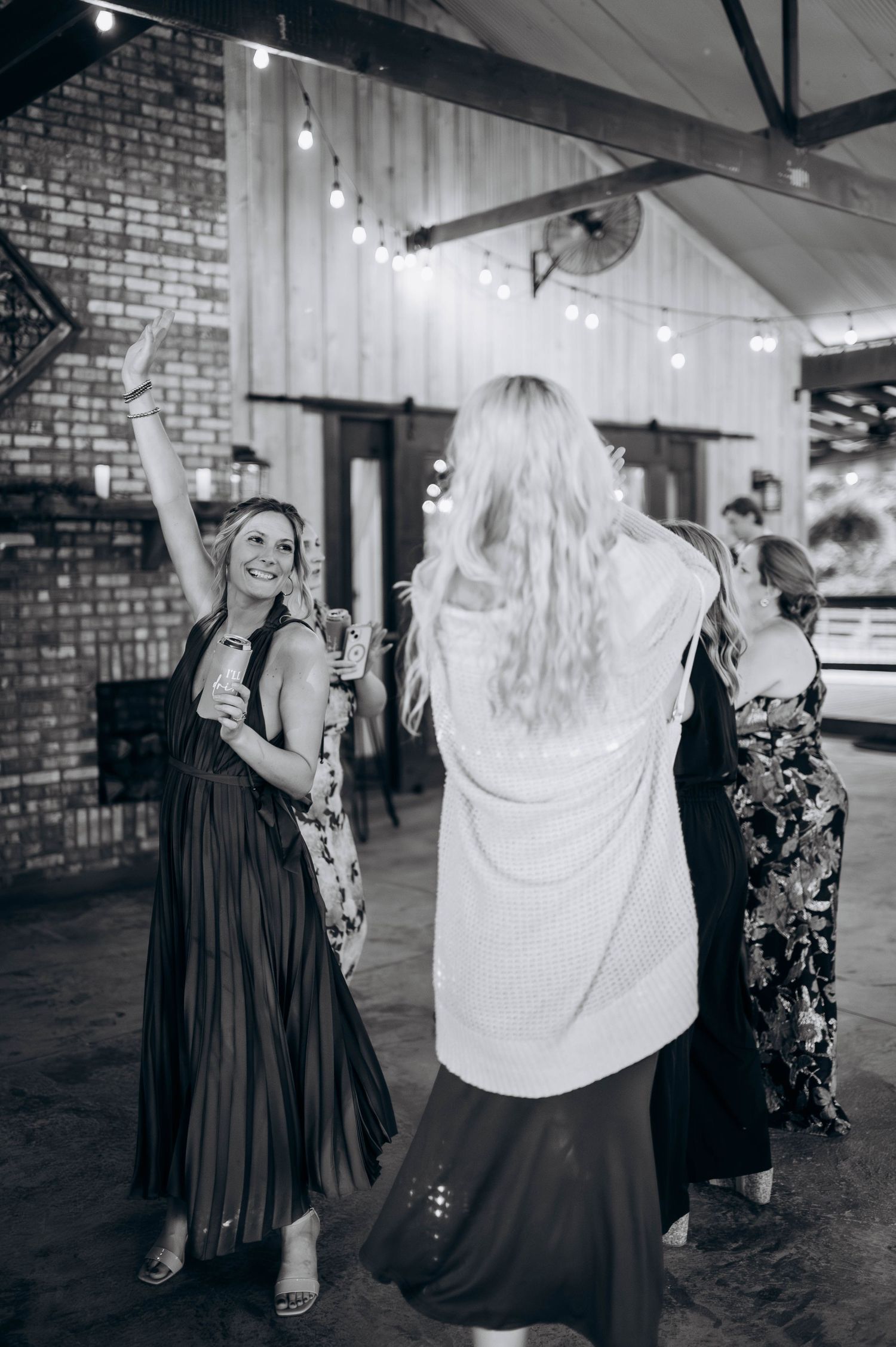 Wedding guests dancing joyfully in a rustic brick venue with string lights overhead.