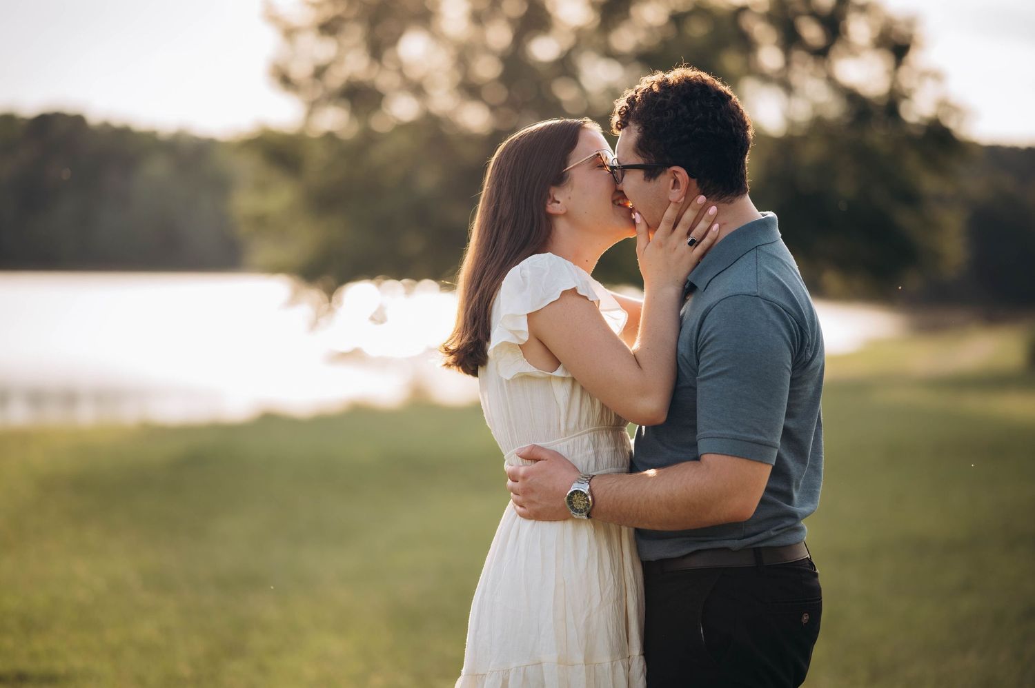 Two people share a tender kiss against a beautiful waterfront backdrop during golden hour.