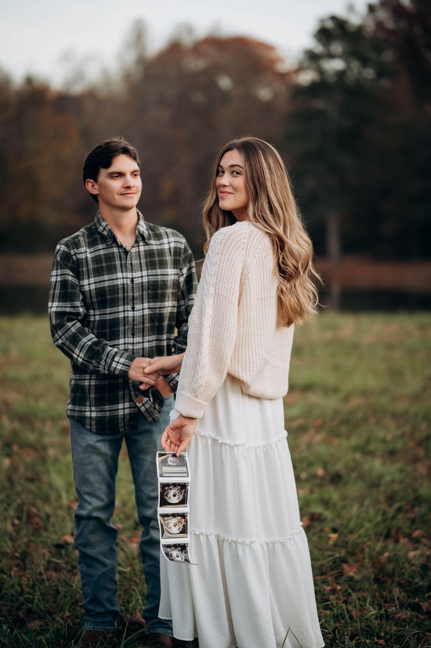 A couple poses with ultrasound photos during their autumn pregnancy announcement session.