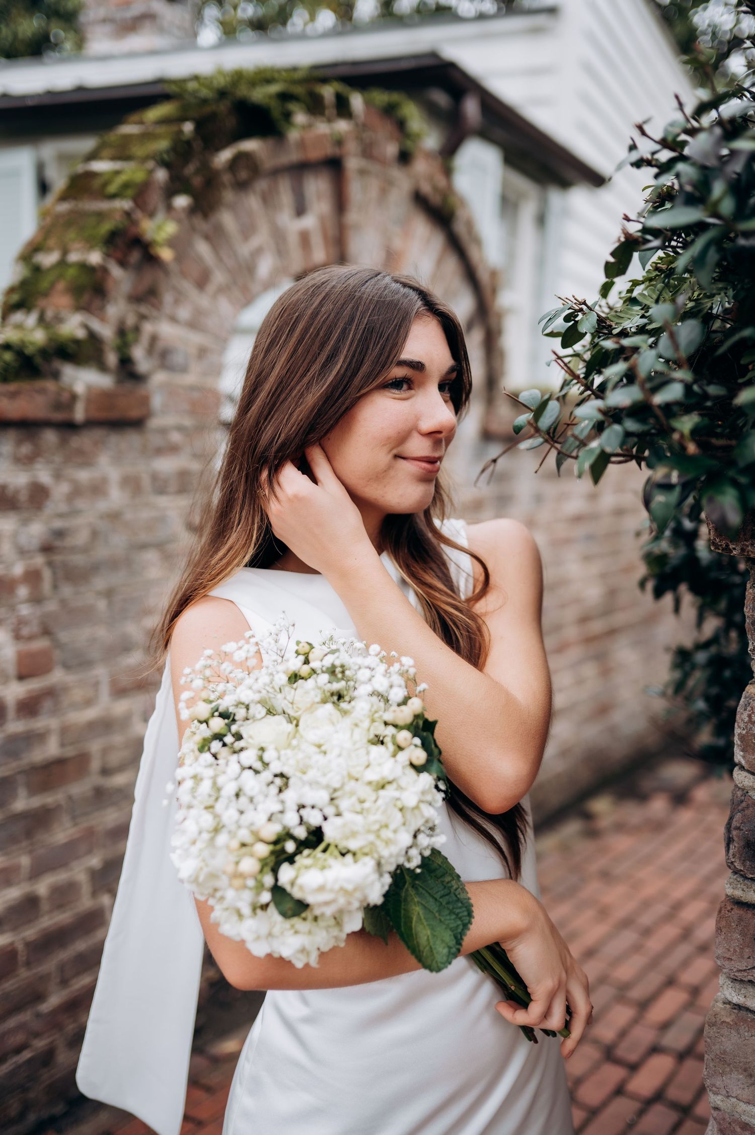 A couple shares intimate moments against a brick wall backdrop with white floral bouquet.