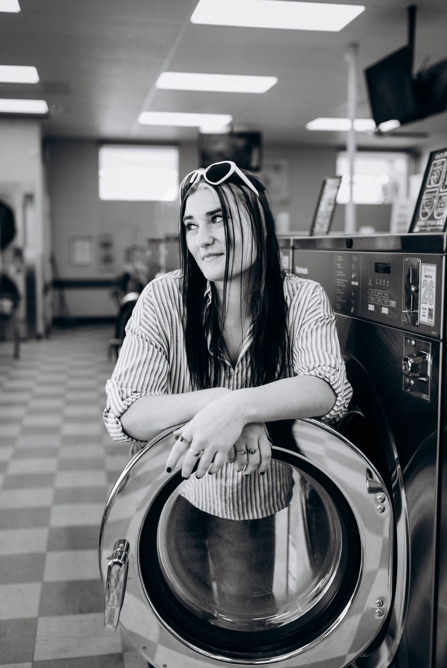 Three black and white photos show someone leaning into an open washing machine in a laundromat with checkered floors.