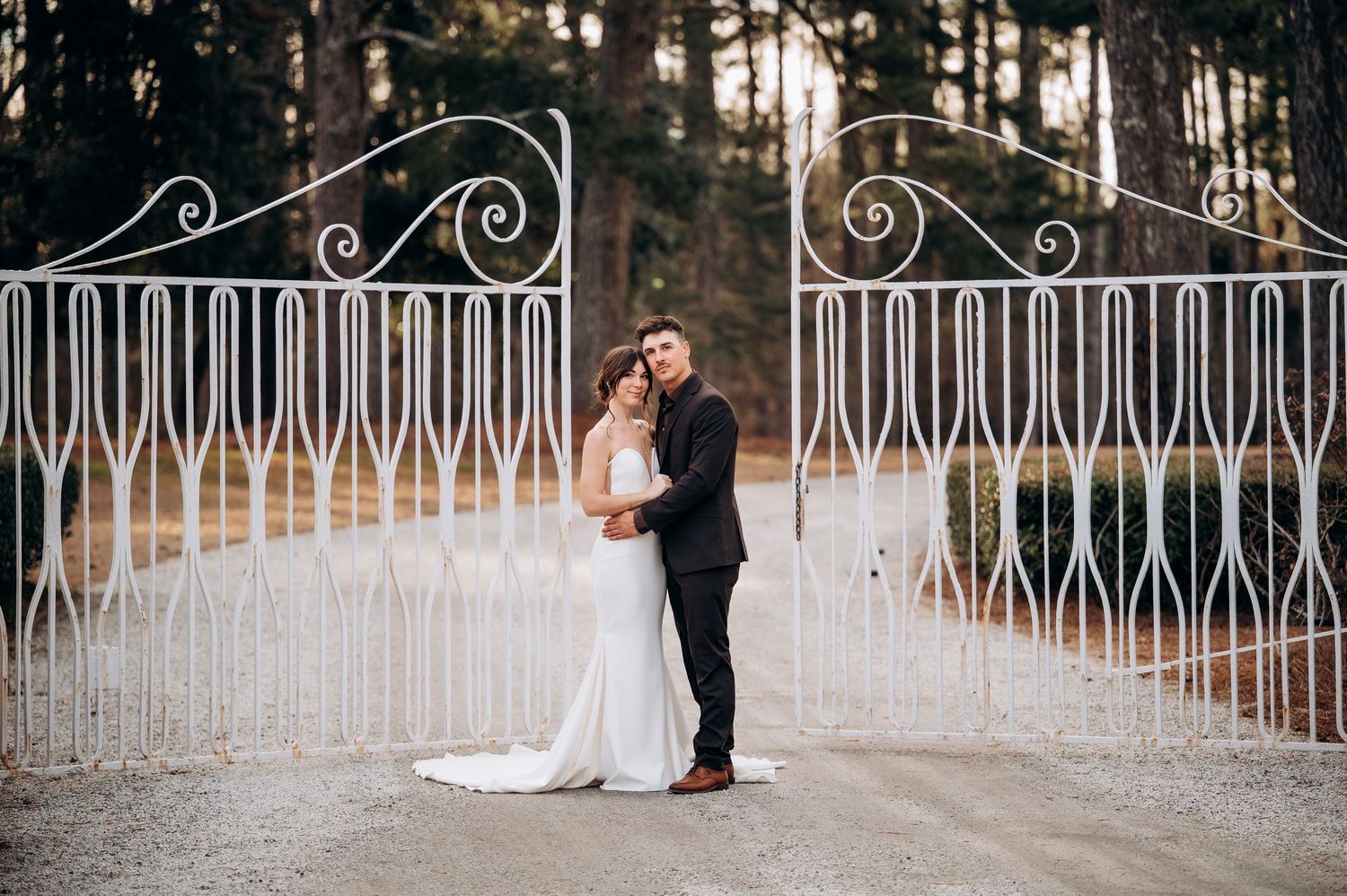 Wedding couple embracing by decorative white iron railings in outdoor setting.