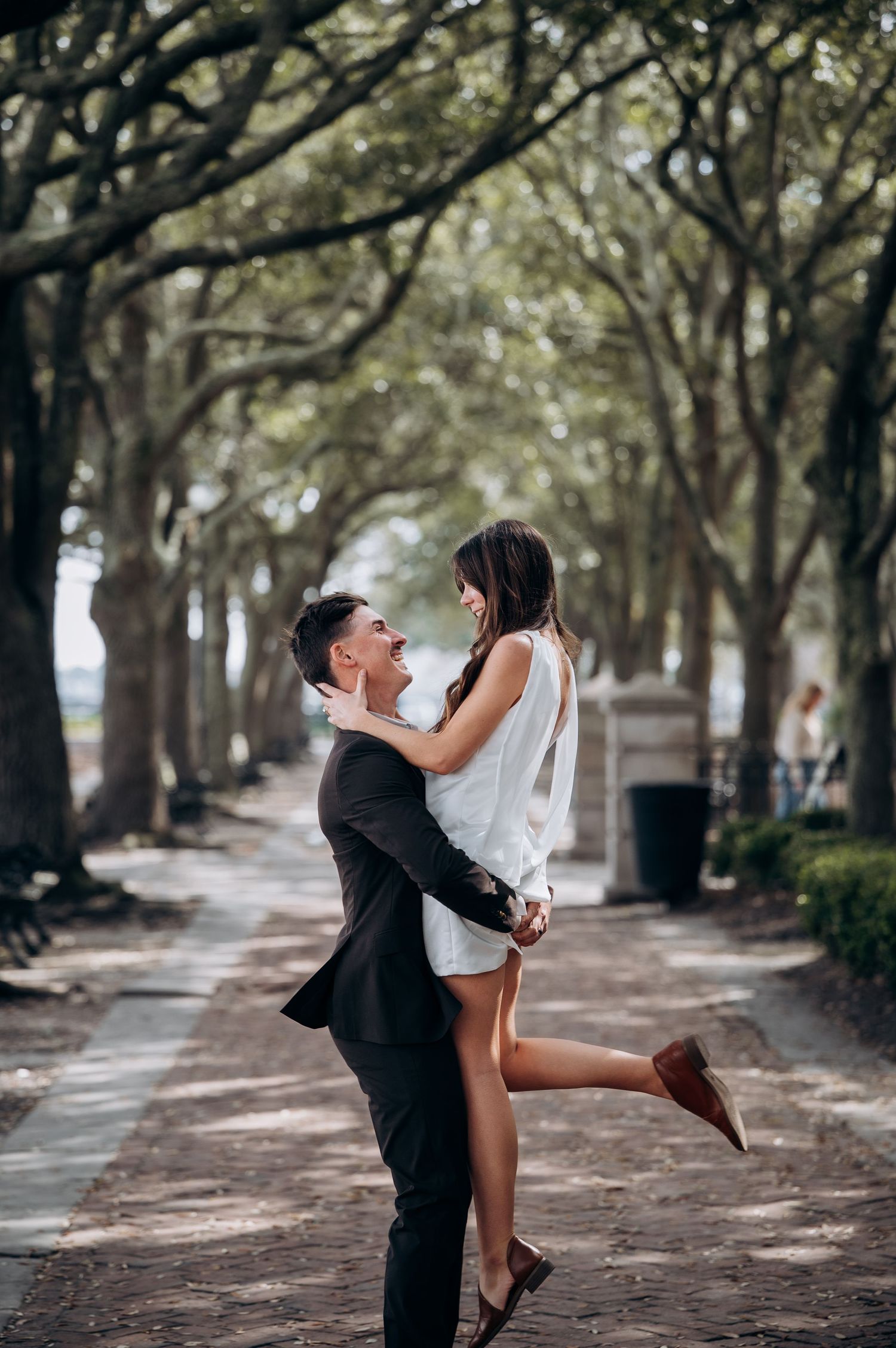 Romantic couple dancing and embracing on tree-lined path with beautiful natural lighting.