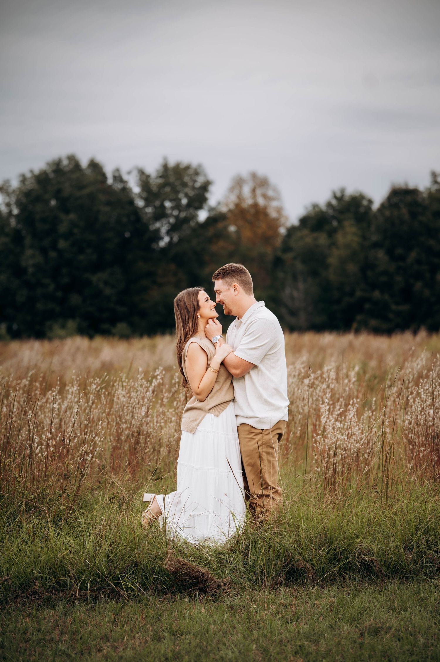 Couple in white clothing sharing romantic moments in tall grass field during golden hour.