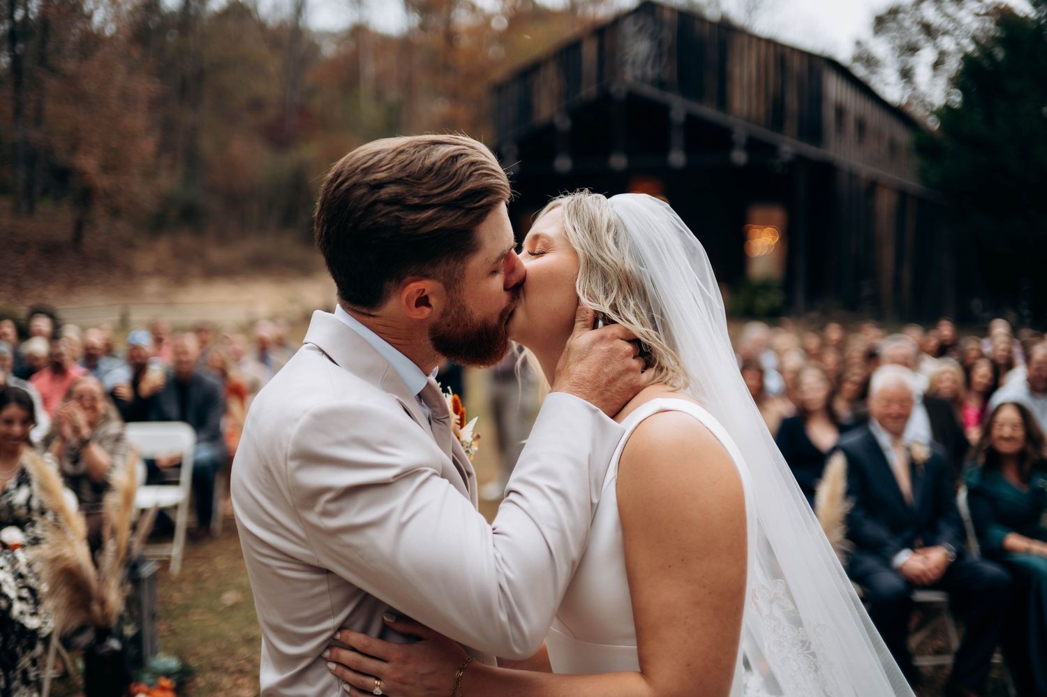 Wedding ceremony kiss with guests watching in outdoor venue.