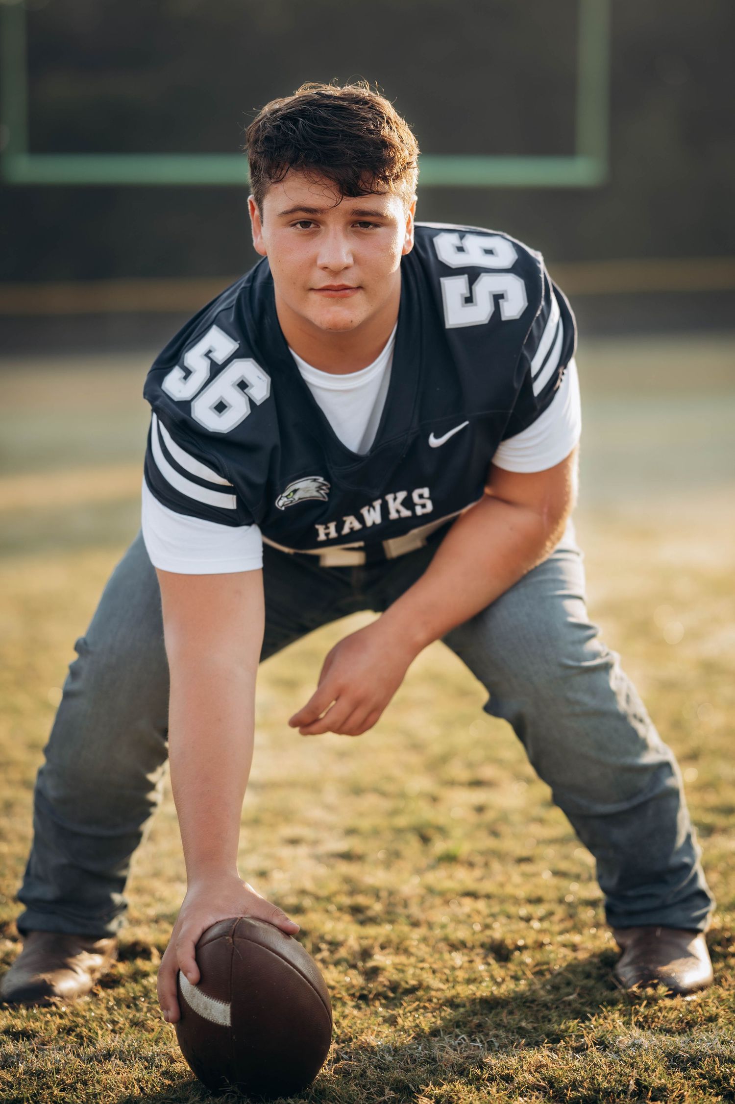 Close-up shot of football player crouching with ball on grass field during golden hour.