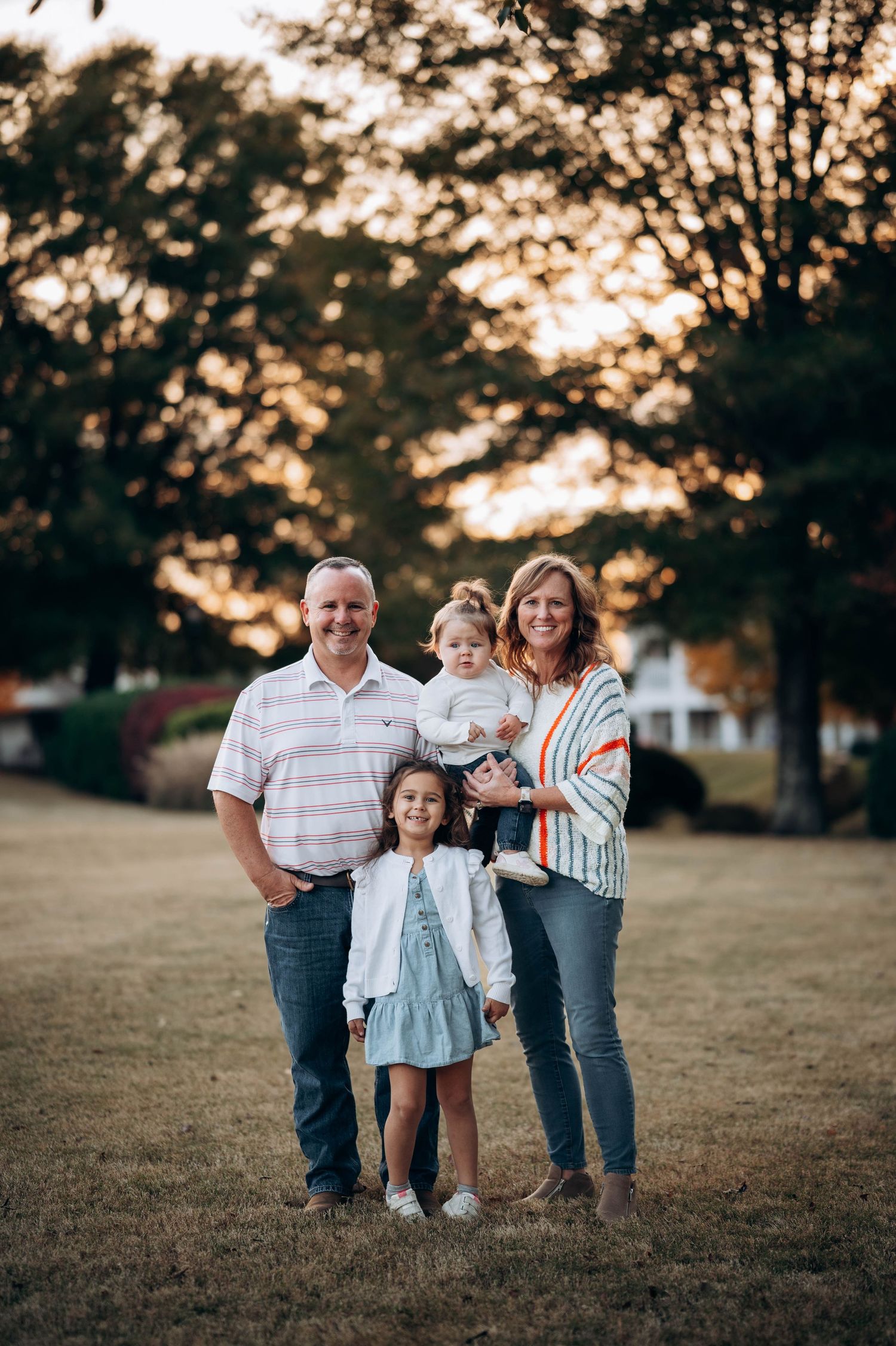 Family portrait taken at golden hour in a grassy field with warm autumn lighting.