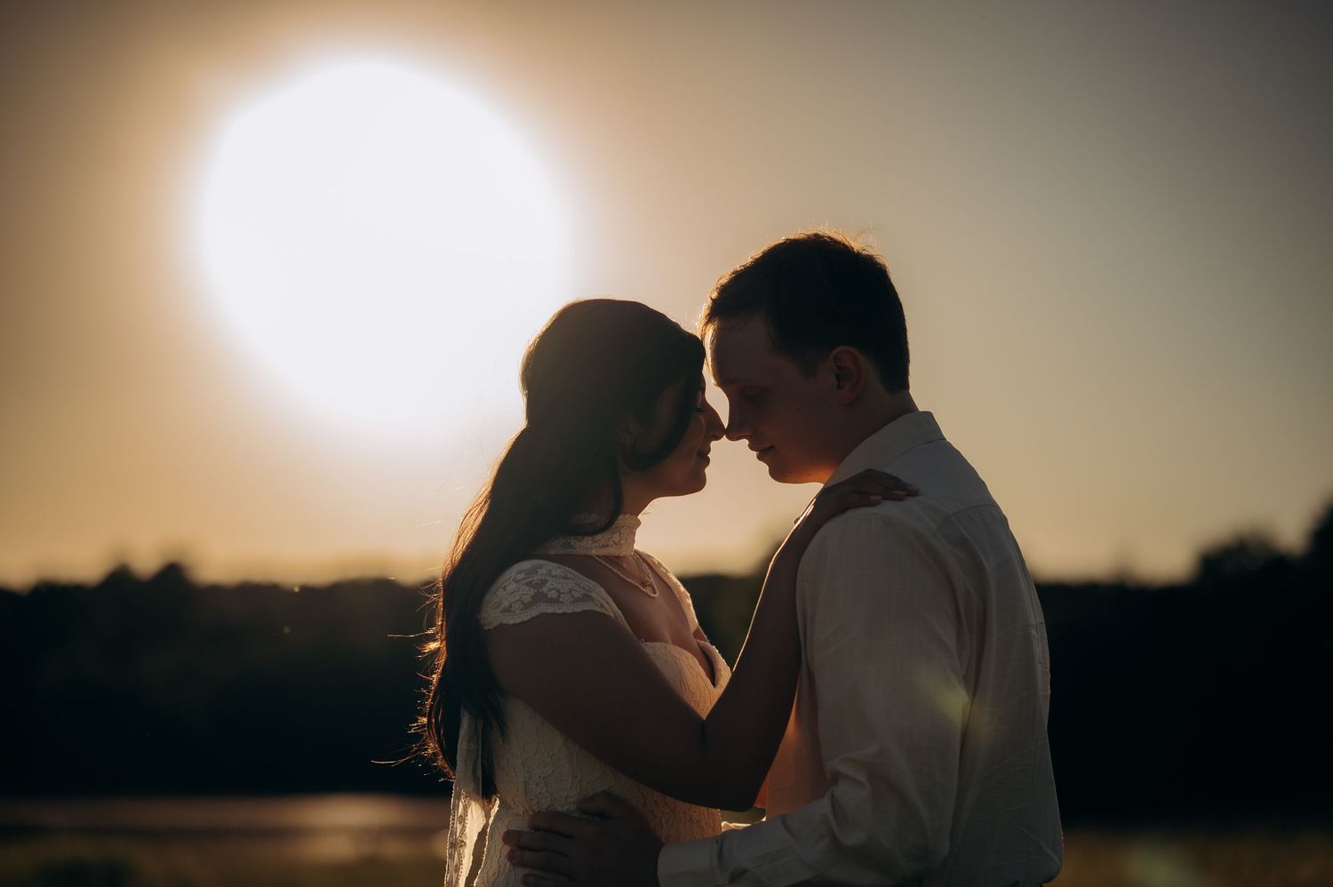 Romantic couple sharing an intimate moment at sunset, silhouetted against a glowing golden sky.