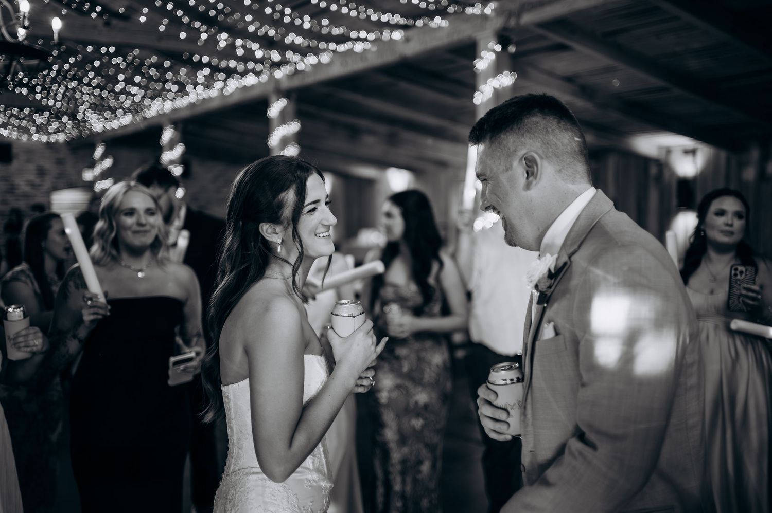 Black and white photo of bride and groom sharing intimate dance moment at wedding reception under string lights.