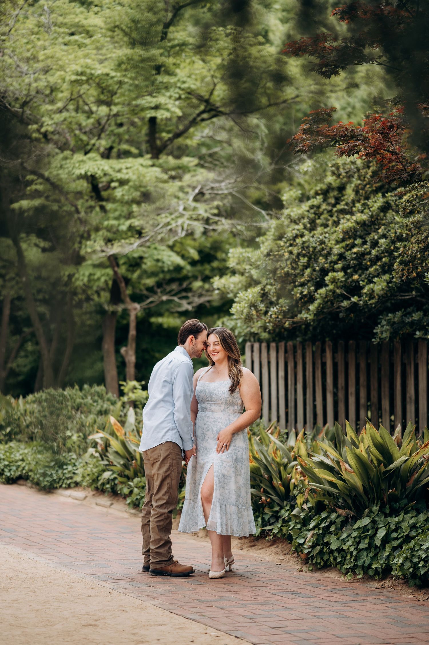 Couple sharing a tender moment on a brick path surrounded by lush green garden foliage.