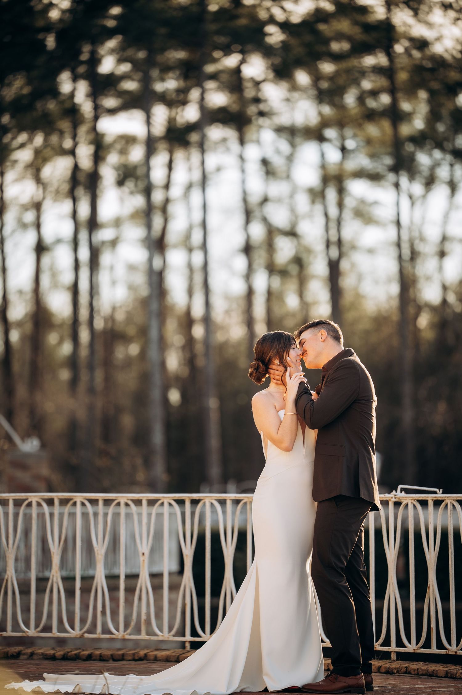 A couple shares a romantic moment on an outdoor terrace with pine trees in the background.