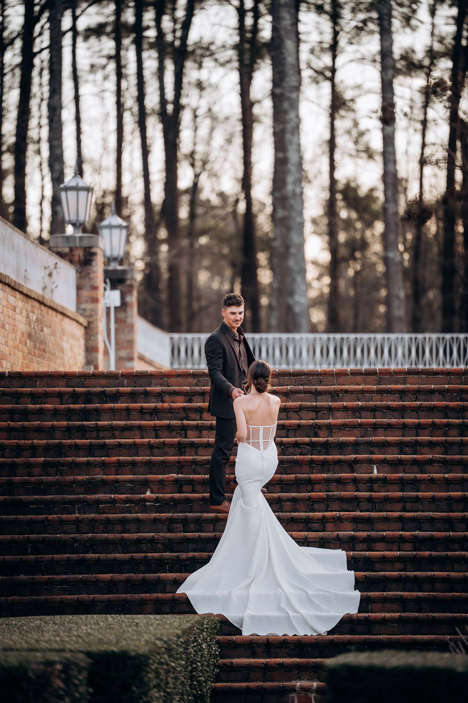 Bride in flowing white gown poses dramatically on grand brick staircase.