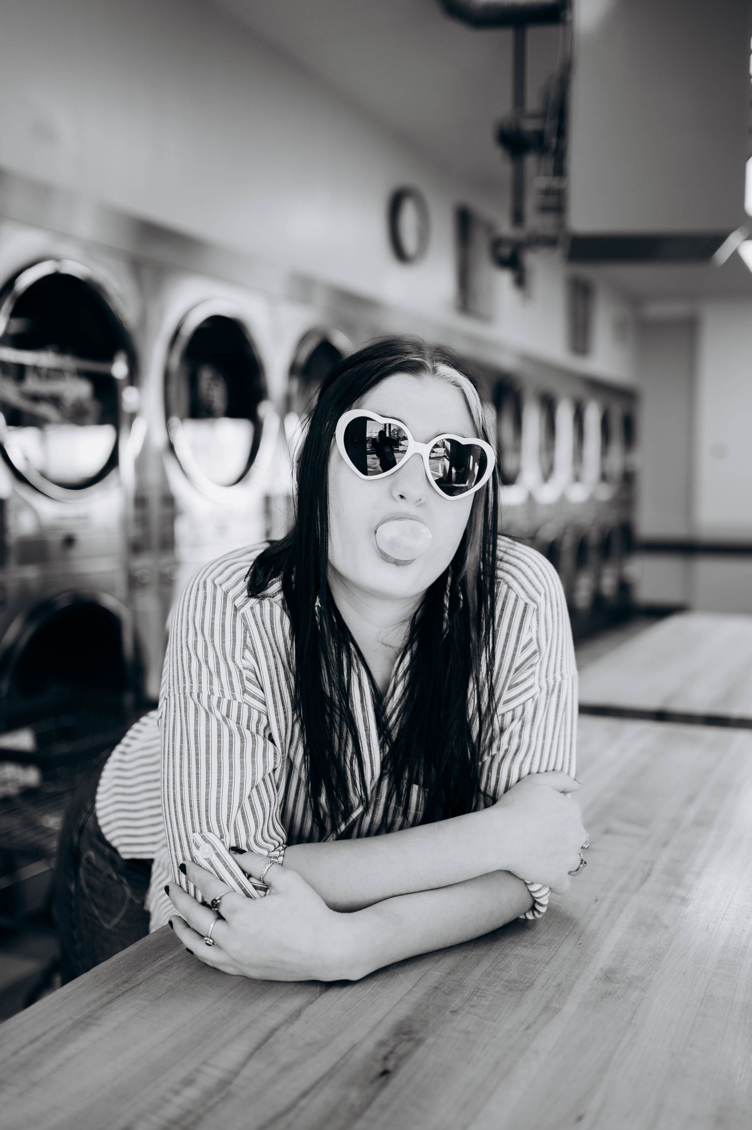 Black and white photo series showing a person in striped shirt and sunglasses reclining on a counter in a laundromat.