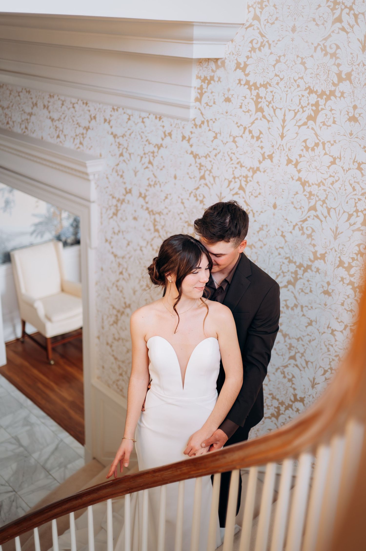 Couple shares intimate moment on vintage staircase with decorative wallpaper.