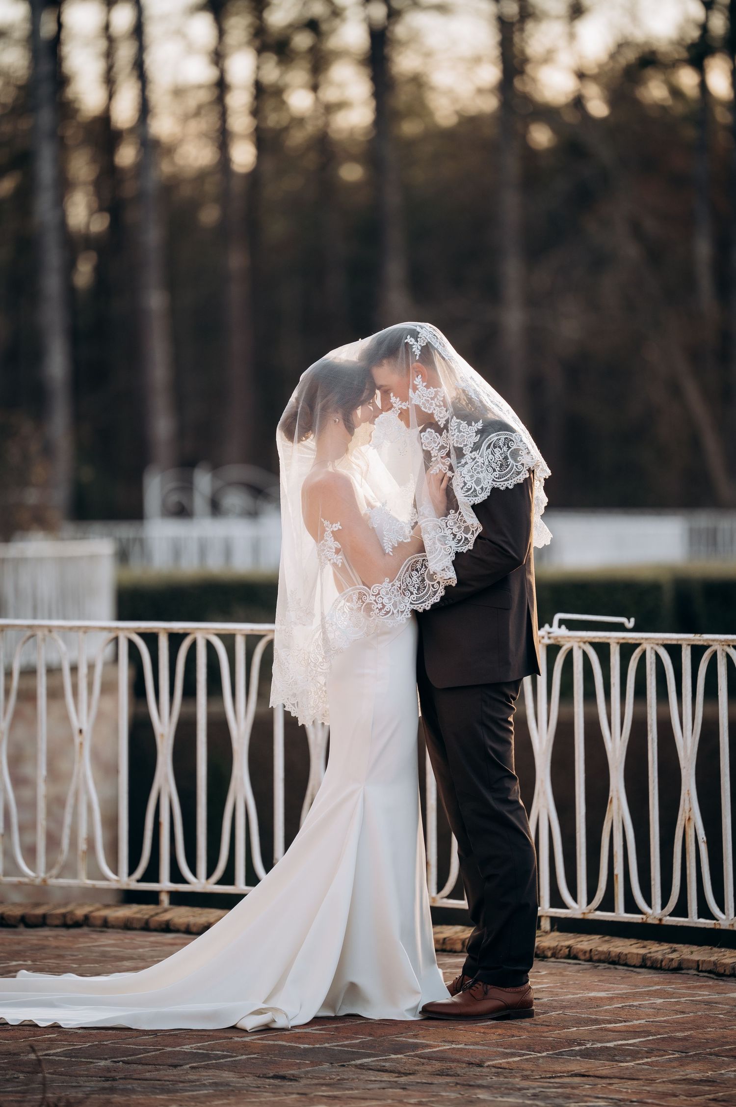 Romantic silhouettes against decorative white railing during sunset wedding shoot.