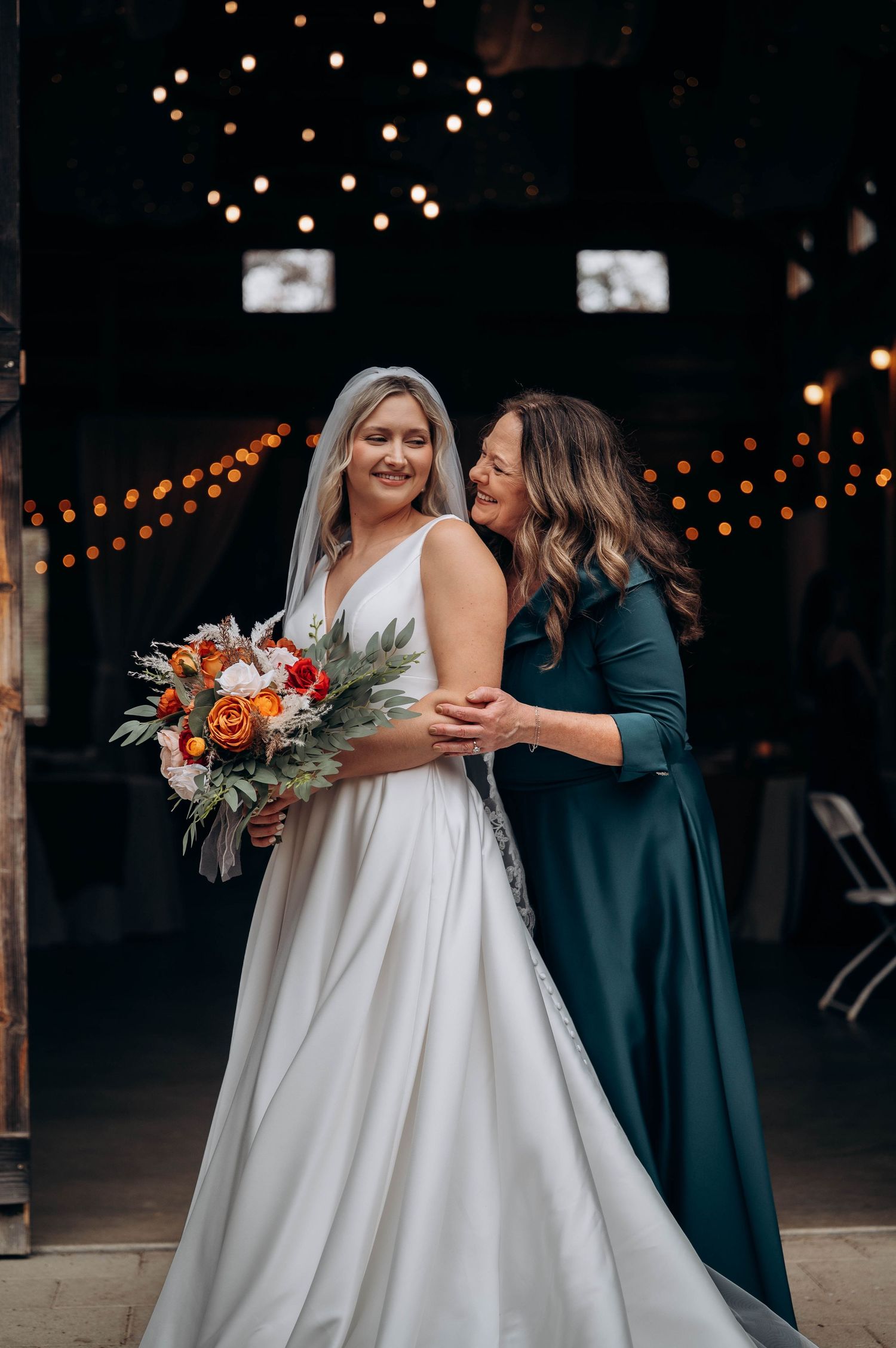 Wedding reception scene with string lights and bride holding autumn-colored bouquet.