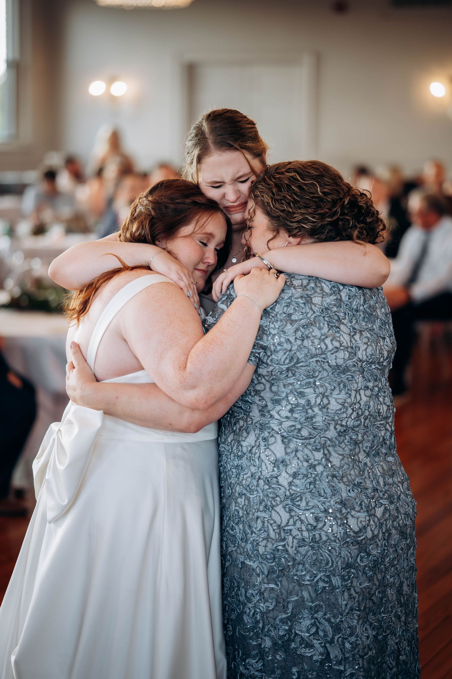 Emotional group hug shared during wedding reception in elegant venue.