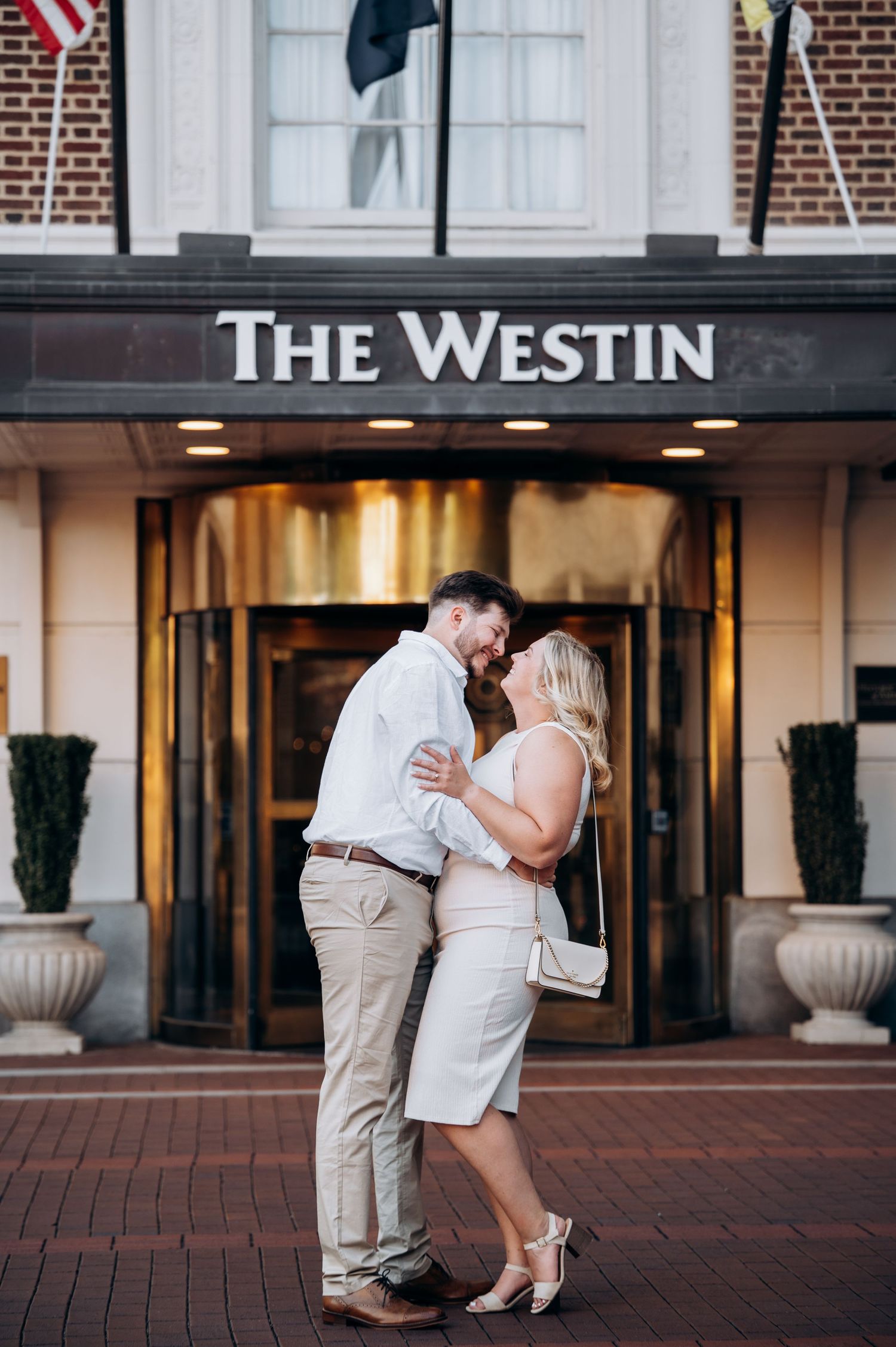 Couple embracing and smiling outside The Westin hotel entrance on a brick sidewalk.
