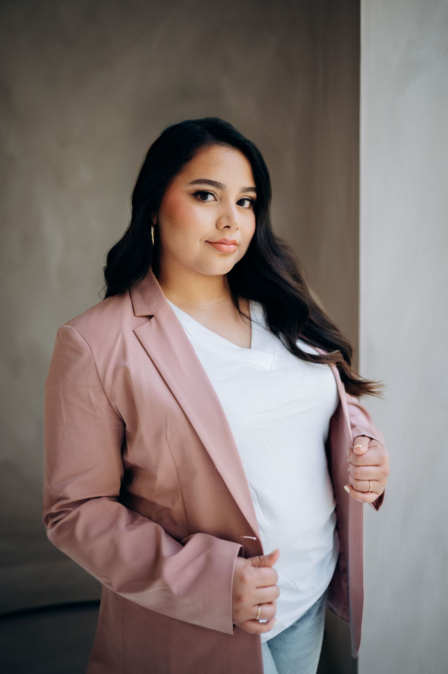 Professional portrait of someone wearing a dusty pink blazer and white top against a neutral background.