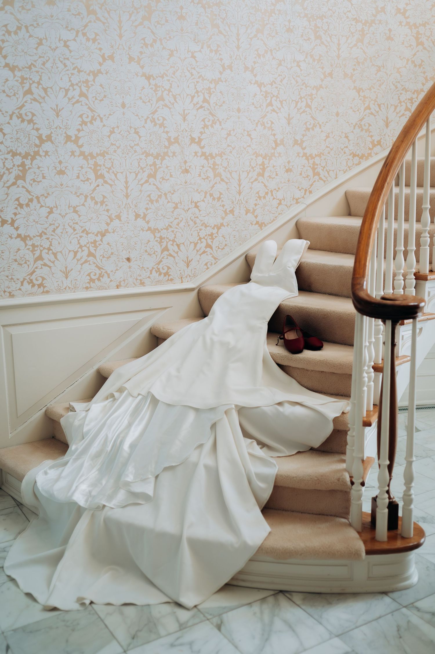 White wedding gown draped elegantly on a curved staircase with ornate wallpaper and wooden banister.