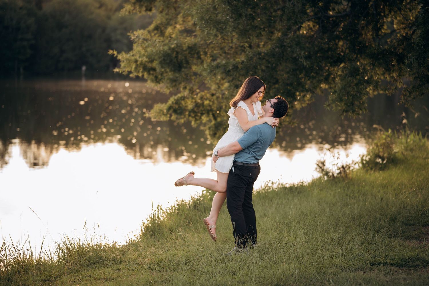 A romantic lakeside photoshoot features a couple in an intimate embrace during sunset.