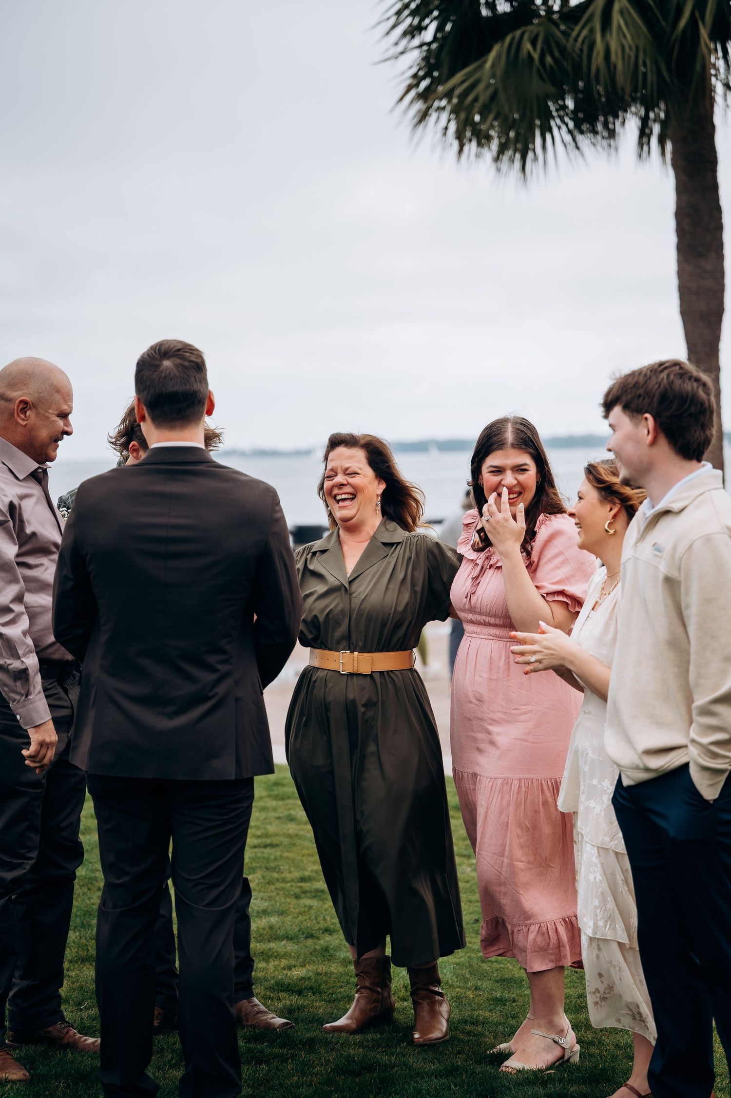 Wedding guests gathered outdoors by the water sharing excited reactions and laughter.