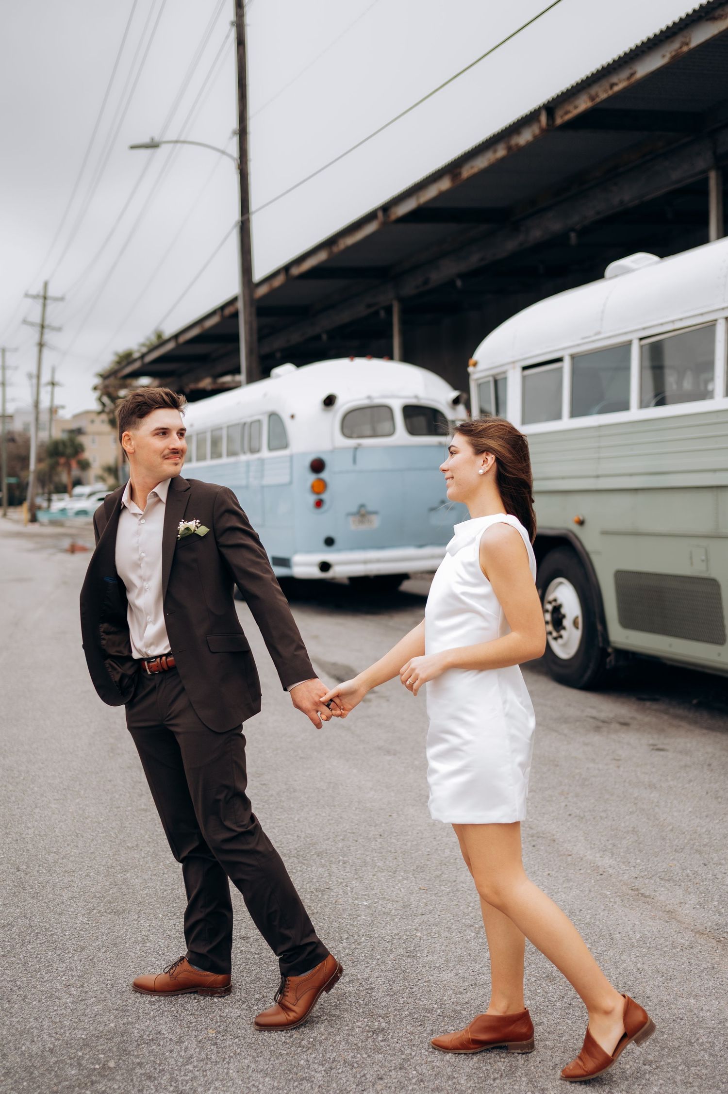 Playful couple dancing near vintage cars in an industrial setting.