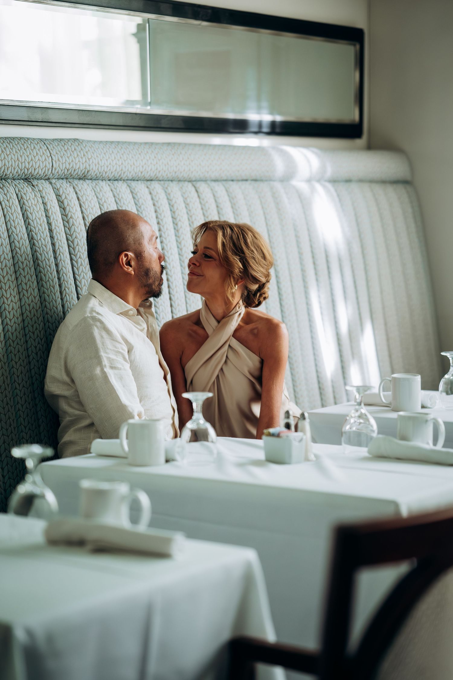 Couple sharing an intimate moment seated at a white tablecloth restaurant booth.