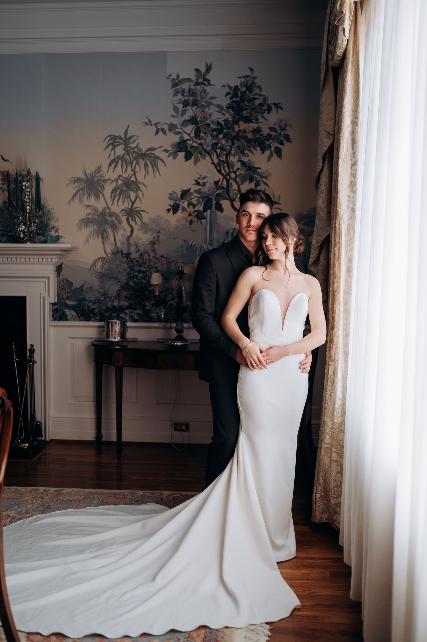 Elegant wedding couple posing in a room with decorative wall murals and flowing white dress.
