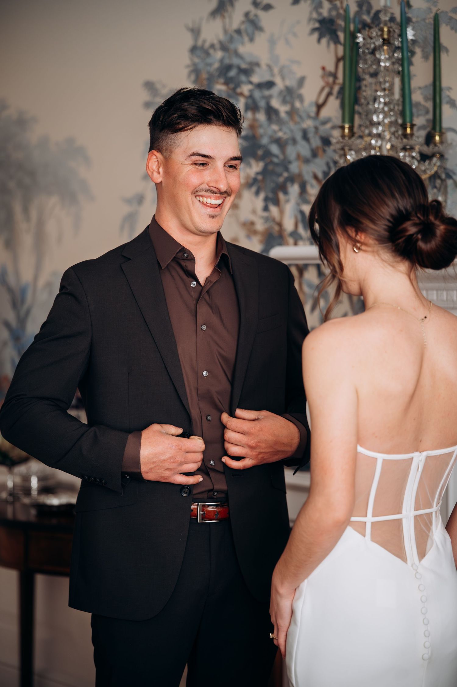 A joyful wedding moment captured indoors with the bride in white and groom in black suit sharing a candid interaction.