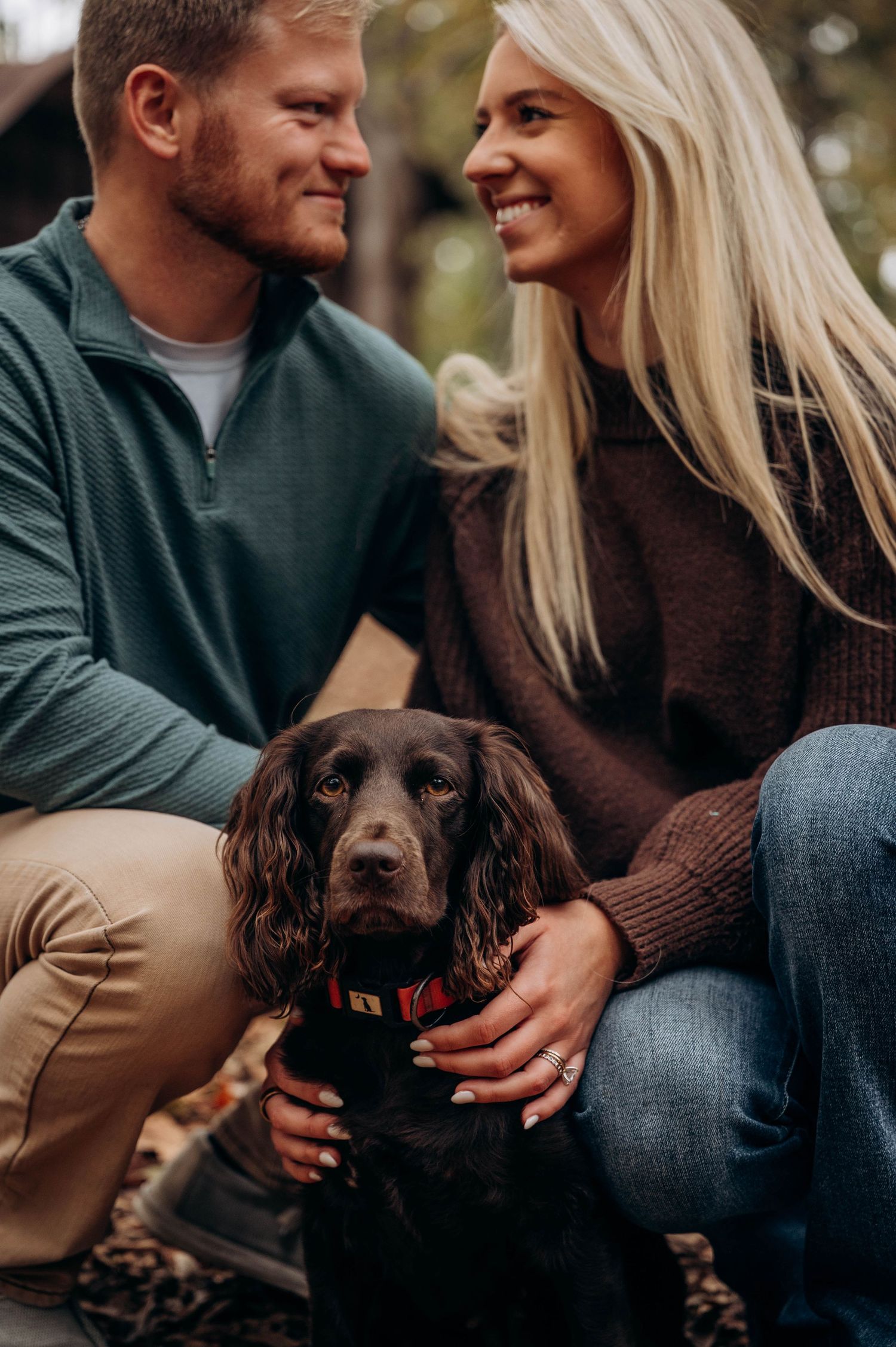 Couple shares intimate moment with their brown dog in casual fall attire.