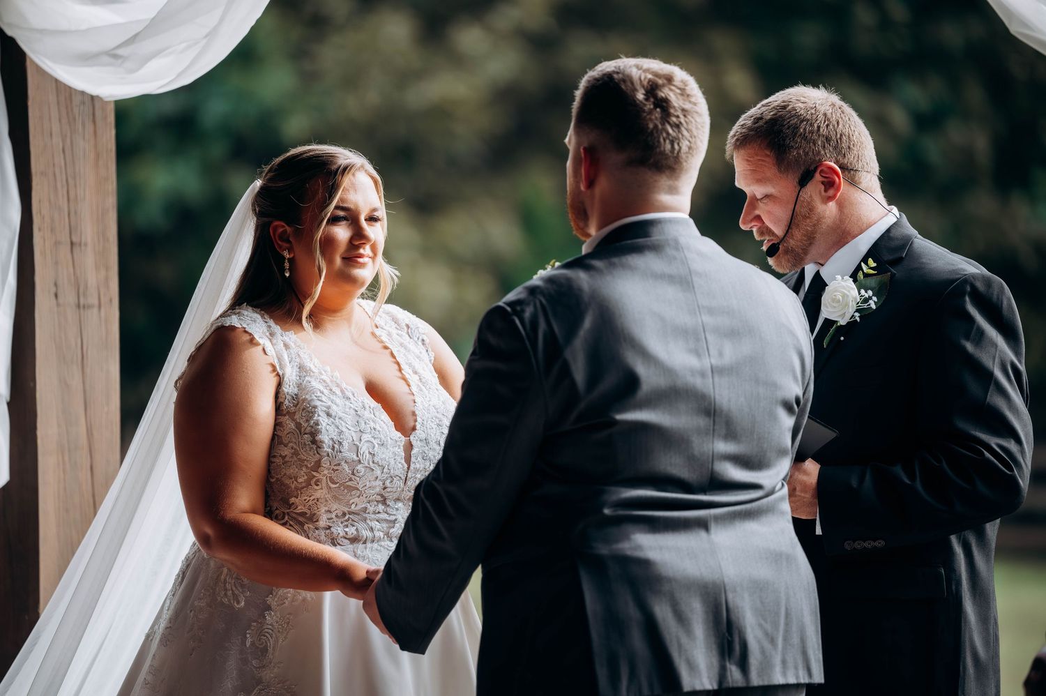 Wedding ceremony under covered pavilion with white drapes and officiant.