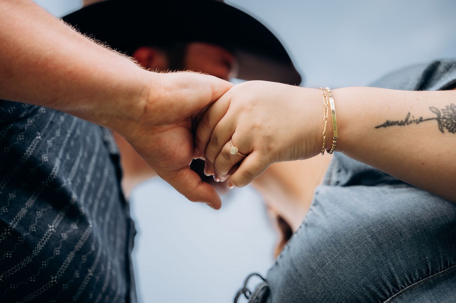 Couple holding hands showing a black ring and gold bracelet with a small tattoo on the woman's wrist.