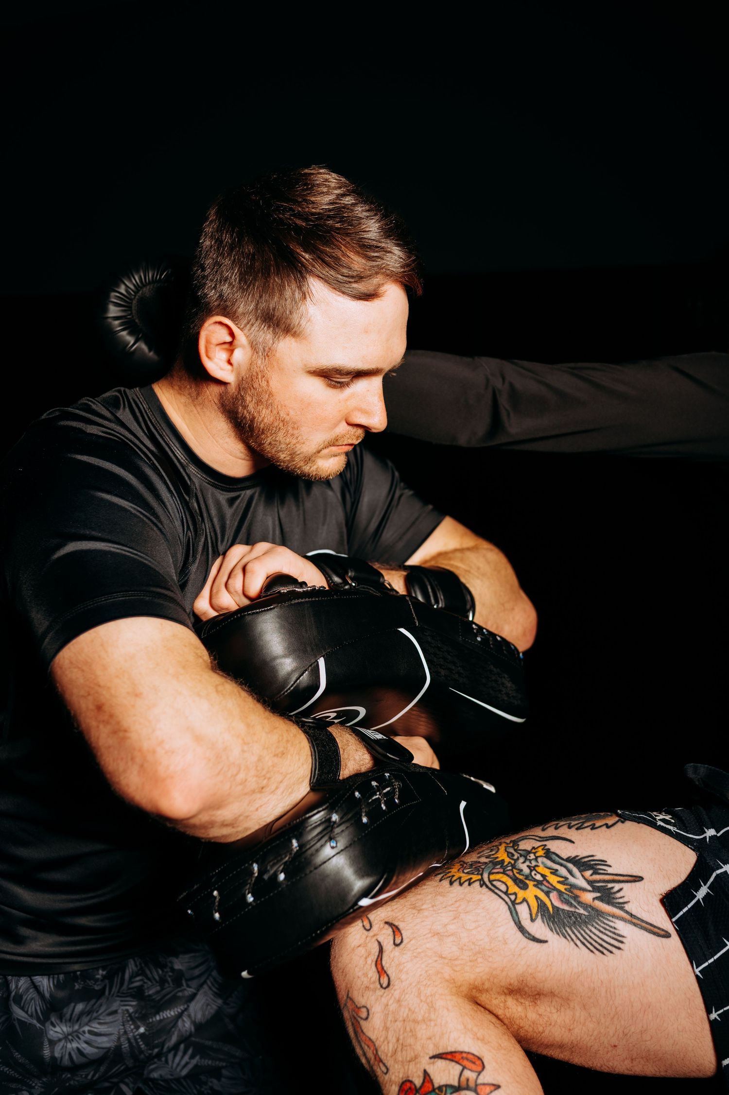 A person in a black t-shirt works on a tattoo design while wearing protective gloves in a dark studio setting.
