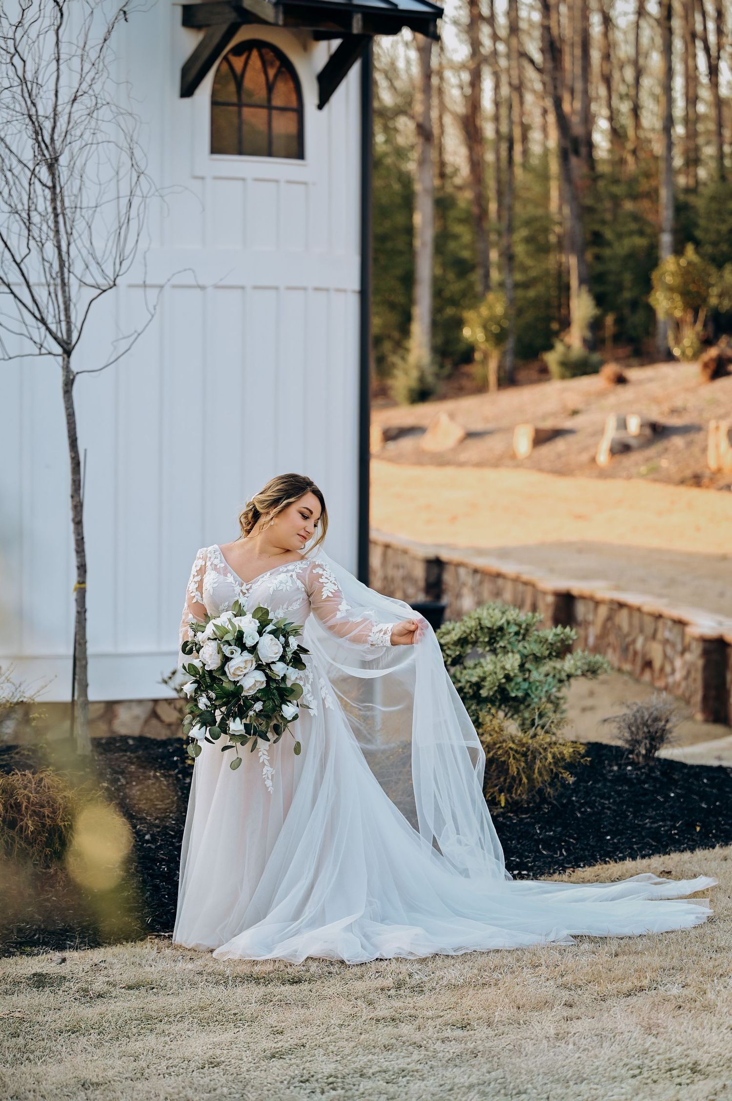 Elegant white wedding gown photographed against rustic chapel exterior.
