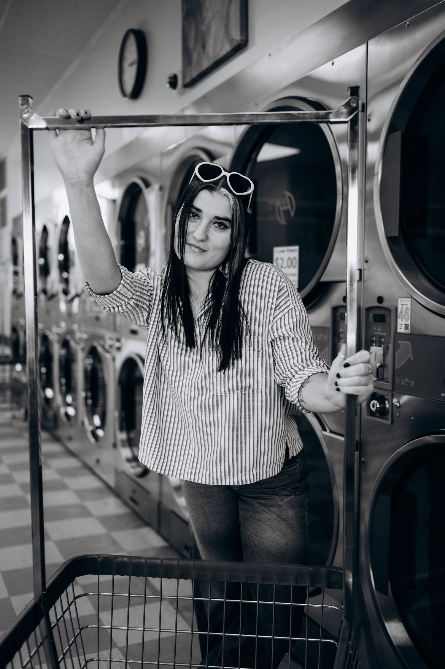 Black and white portrait of someone in striped shirt posing at a laundromat with industrial washing machines.