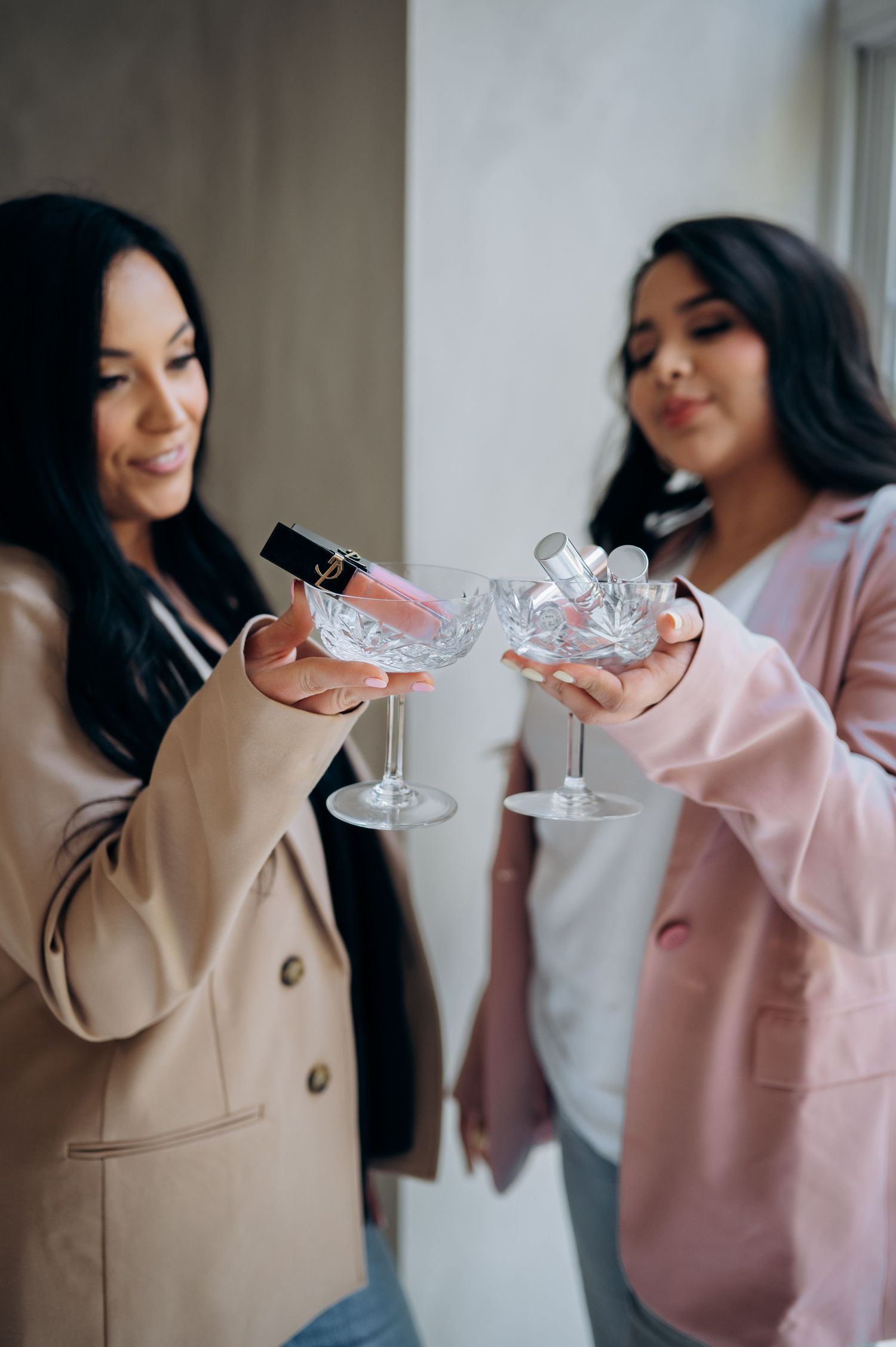 Two friends in blazers clink decorative cocktail glasses together in a celebratory toast.