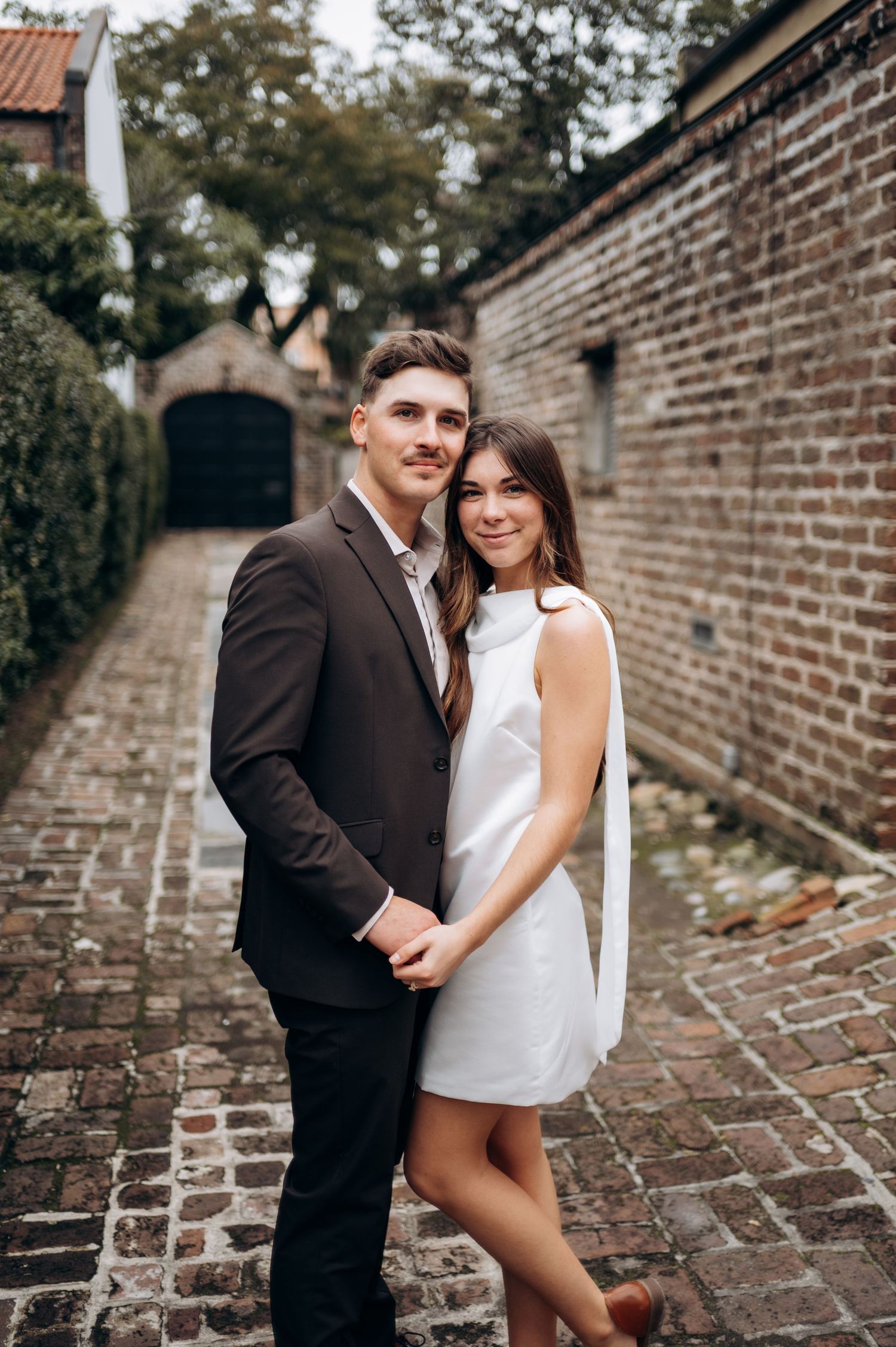 Couple posing playfully along historic brick walls and pathways.