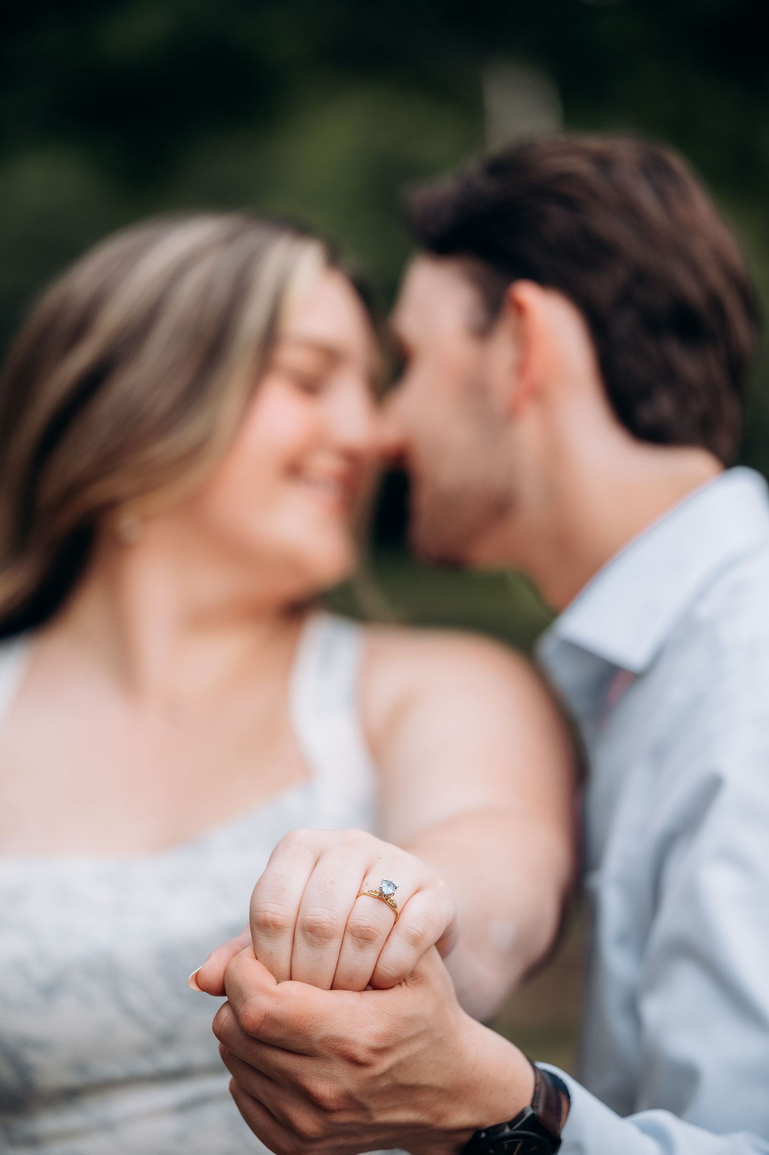 Close-up of couple nearly kissing while showing off diamond engagement ring in foreground.