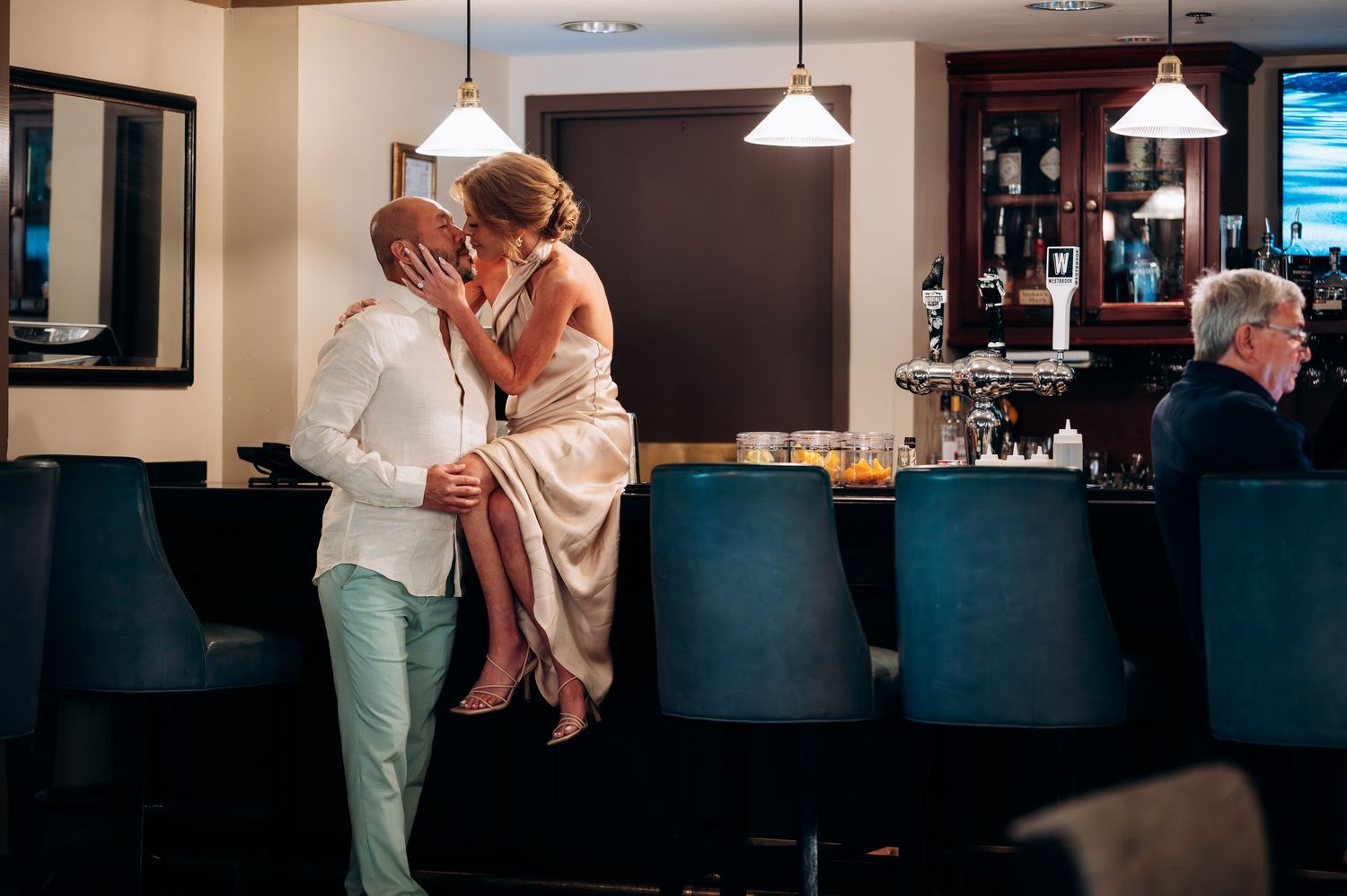 Couple sharing a romantic kiss at an elegant hotel bar with teal velvet chairs.