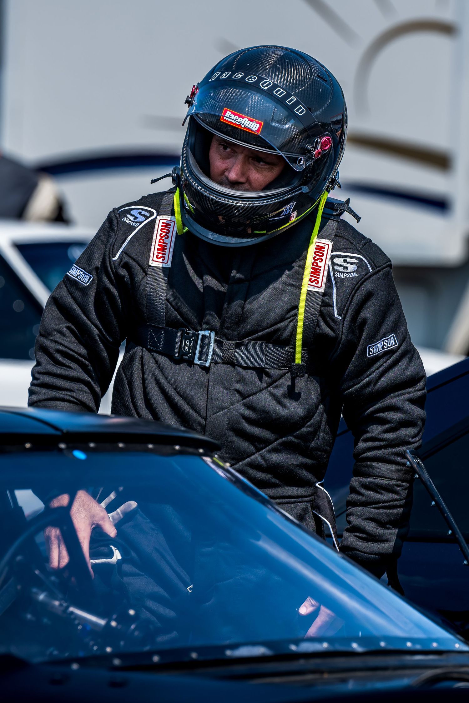Racing crew member in black protective gear checking a blue race car.