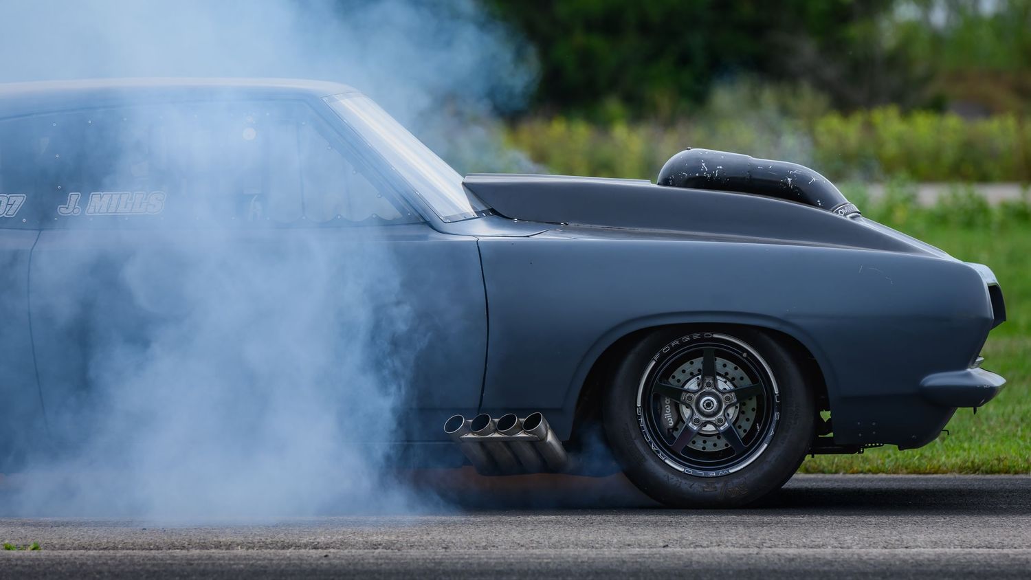 Low angle view of modified classic cars with smoke trails during a drag race.