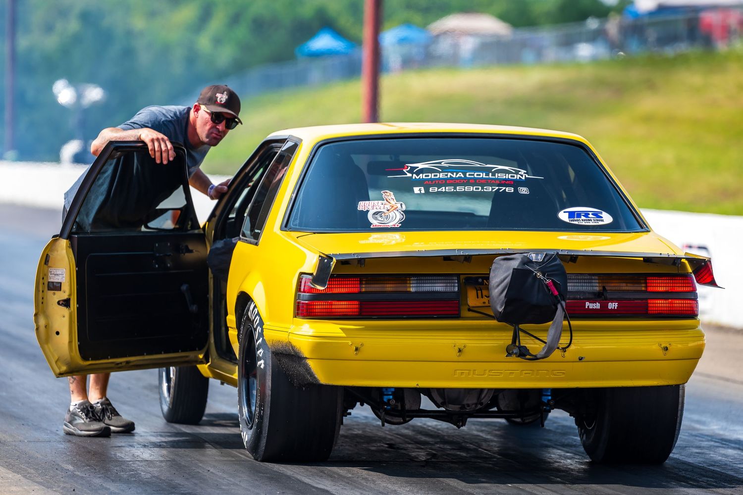 A yellow drag racing car being prepared at the starting line.